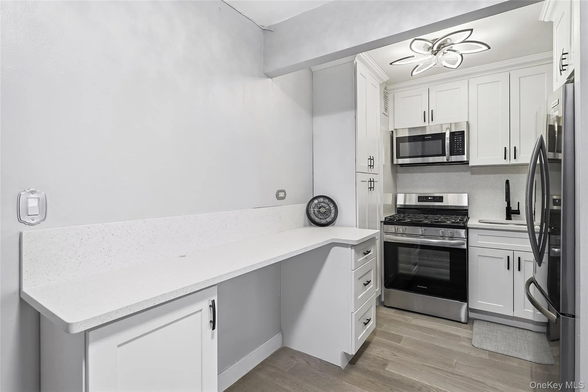 Kitchen featuring stainless steel appliances, white cabinetry, light wood-type flooring, and light stone countertops Kitchen featuring stainless steel appliances, white cabinetry, light wood-type flooring, and light stone countertops