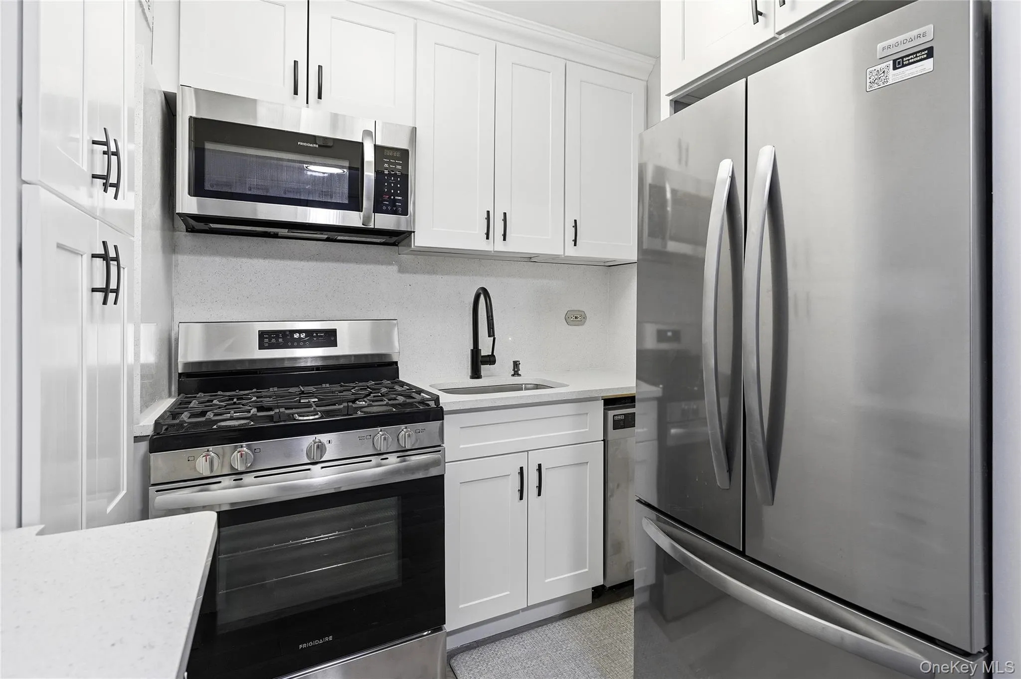 Kitchen with appliances with stainless steel finishes, white cabinets, backsplash, and light stone countertops Kitchen with appliances with stainless steel finishes, white cabinets, backsplash, and light stone countertops