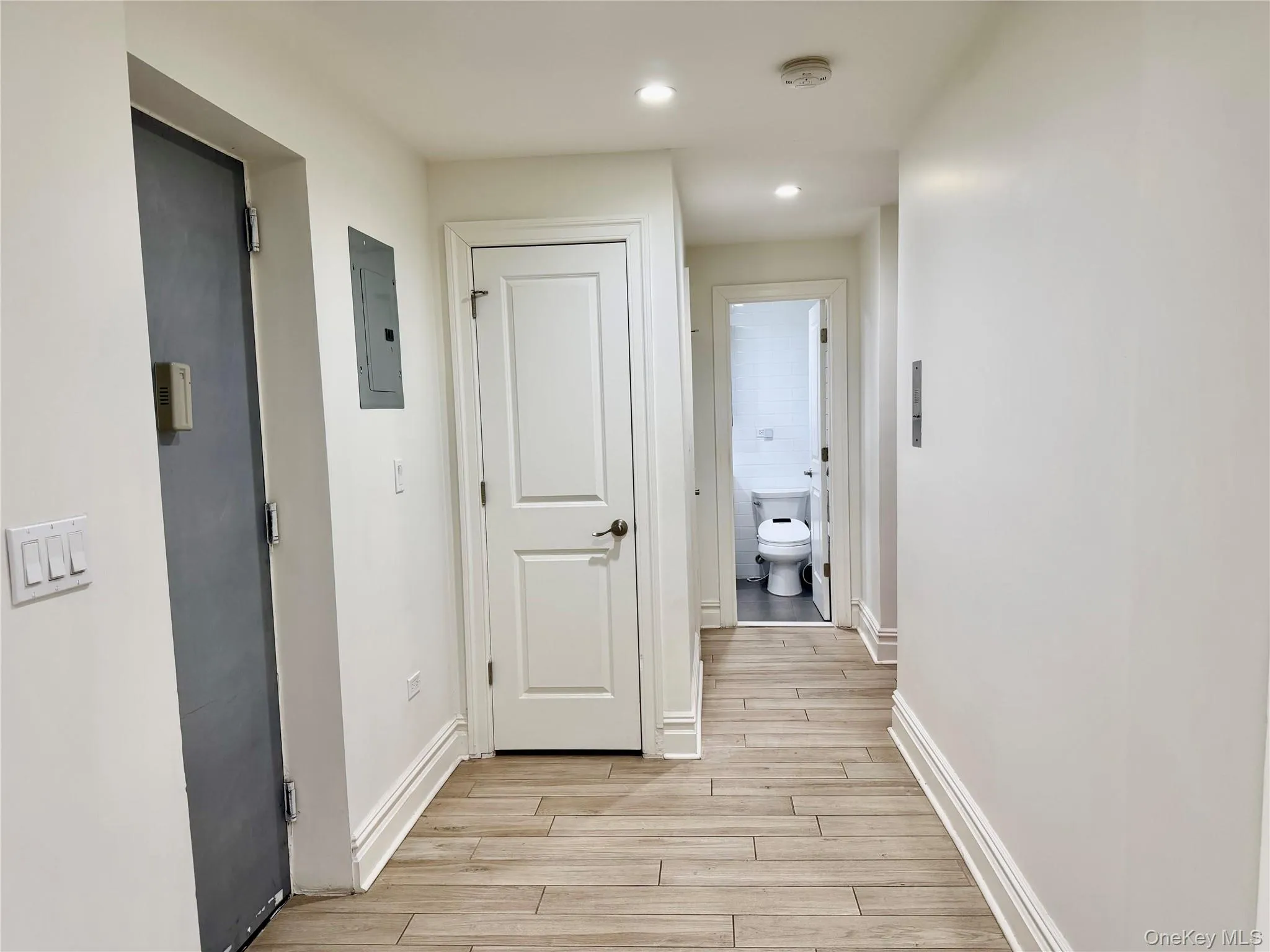 Hallway featuring electric panel, wood-like tiled floors, and recessed lighting Hallway featuring electric panel, wood-like tiled floors, and recessed lighting