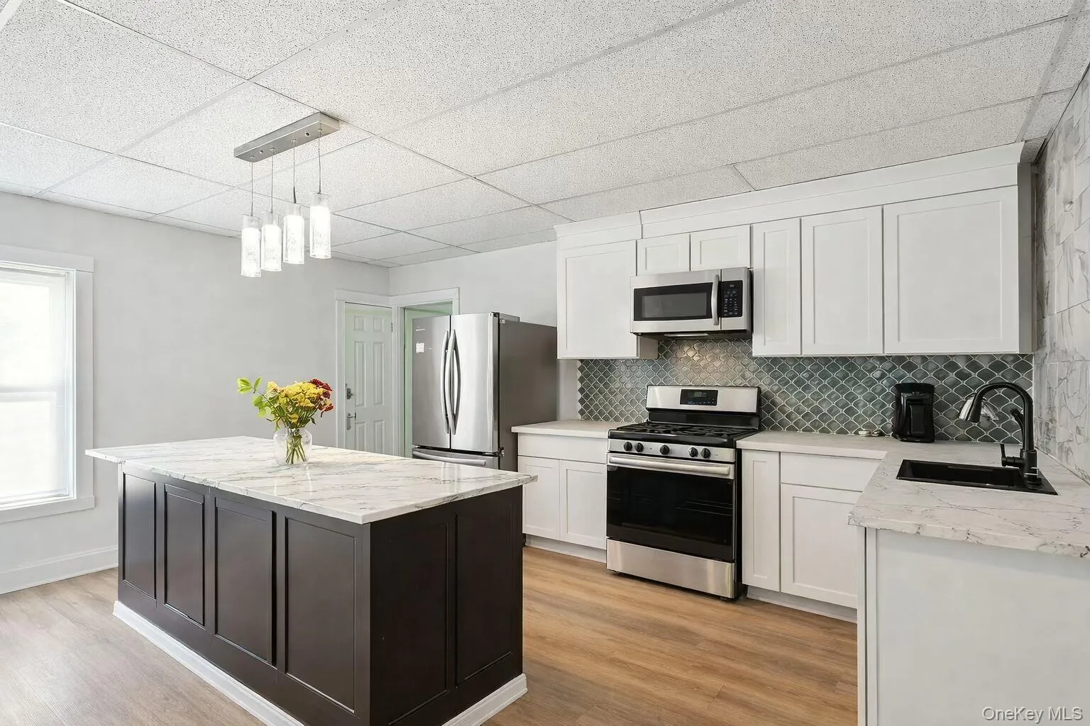 Kitchen featuring a paneled ceiling, appliances with stainless steel finishes, white cabinets, light stone counters, and pendant lighting Kitchen featuring a paneled ceiling, appliances with stainless steel finishes, white cabinets, light stone counters, and pendant lighting