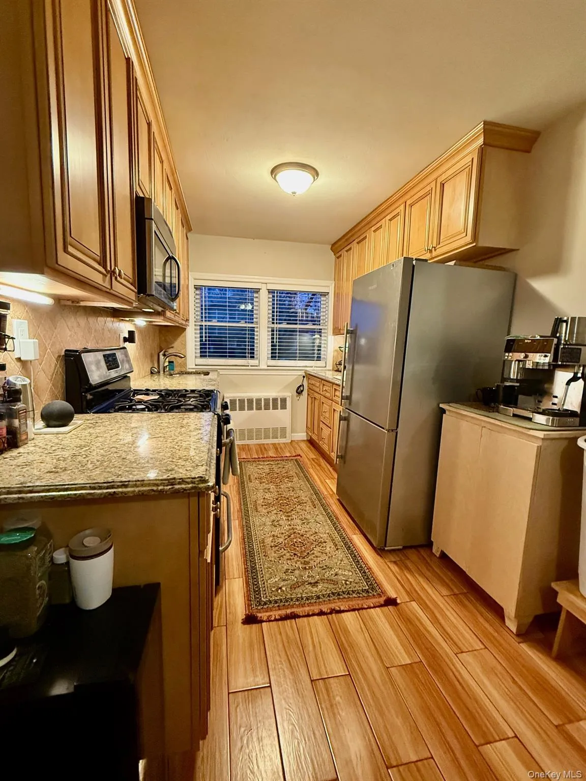 Kitchen featuring stainless steel appliances, light stone counters, light wood-type flooring, and light brown cabinets Kitchen featuring stainless steel appliances, light stone counters, light wood-type flooring, and light brown cabinets