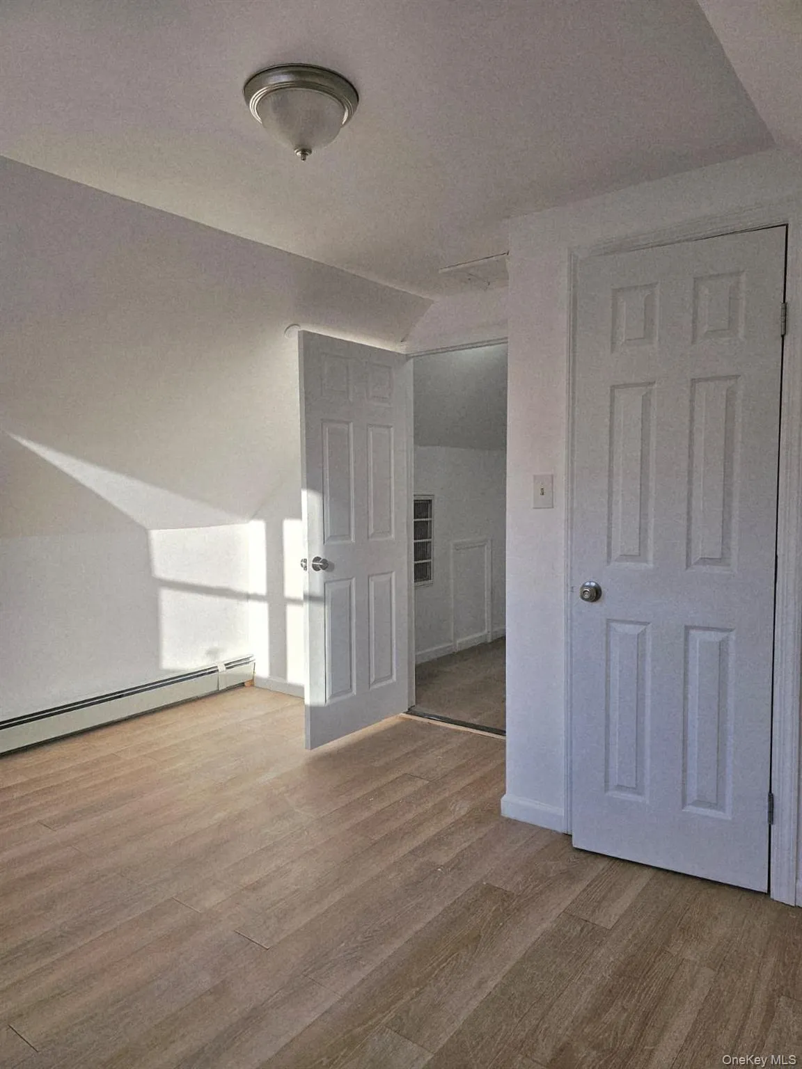 Empty room featuring lofted ceiling, a baseboard heating unit, and light wood-style flooring Empty room featuring lofted ceiling, a baseboard heating unit, and light wood-style flooring