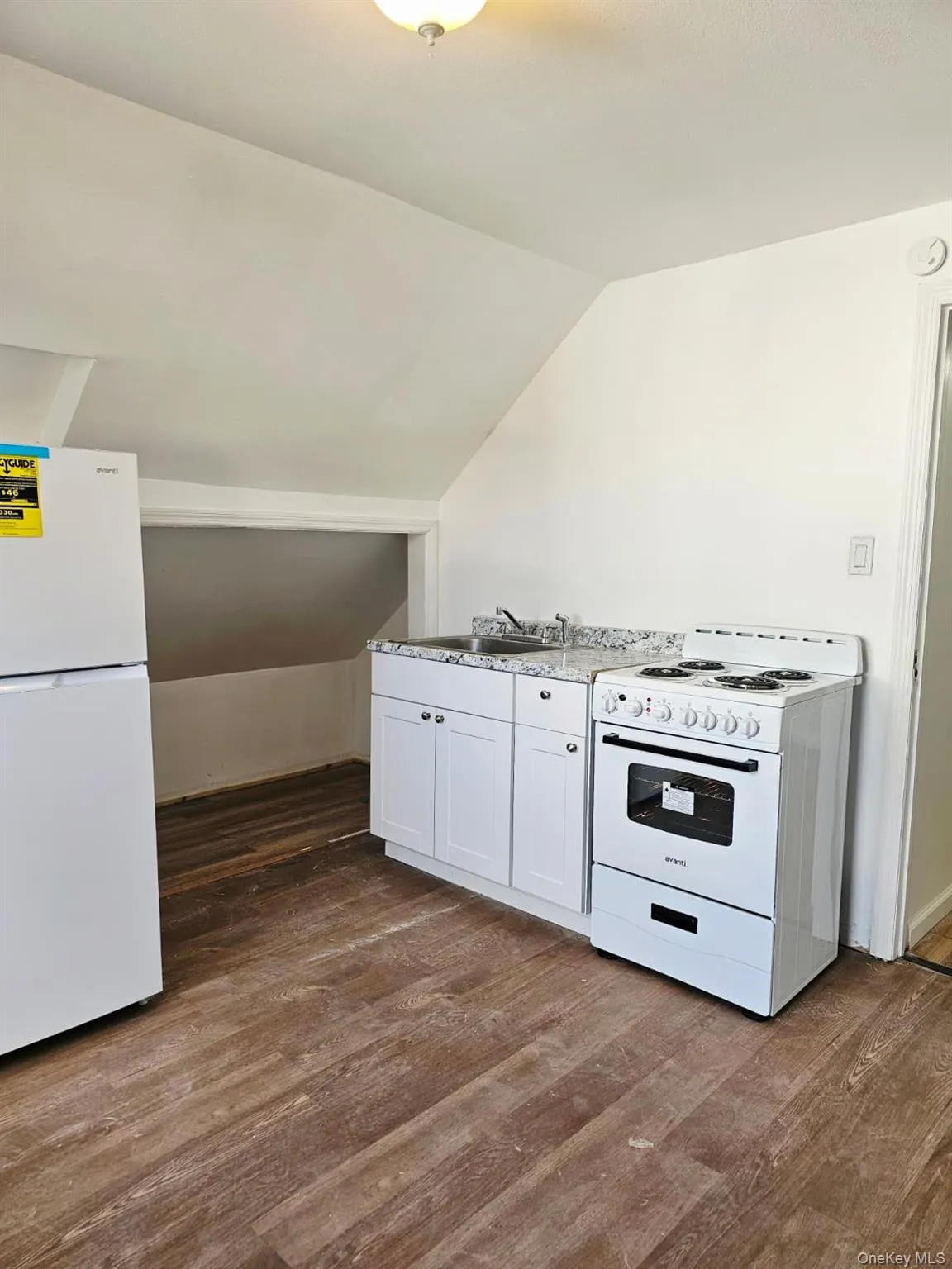 Kitchen featuring white appliances, dark wood-style flooring, white cabinetry, and vaulted ceiling Kitchen featuring white appliances, dark wood-style flooring, white cabinetry, and vaulted ceiling