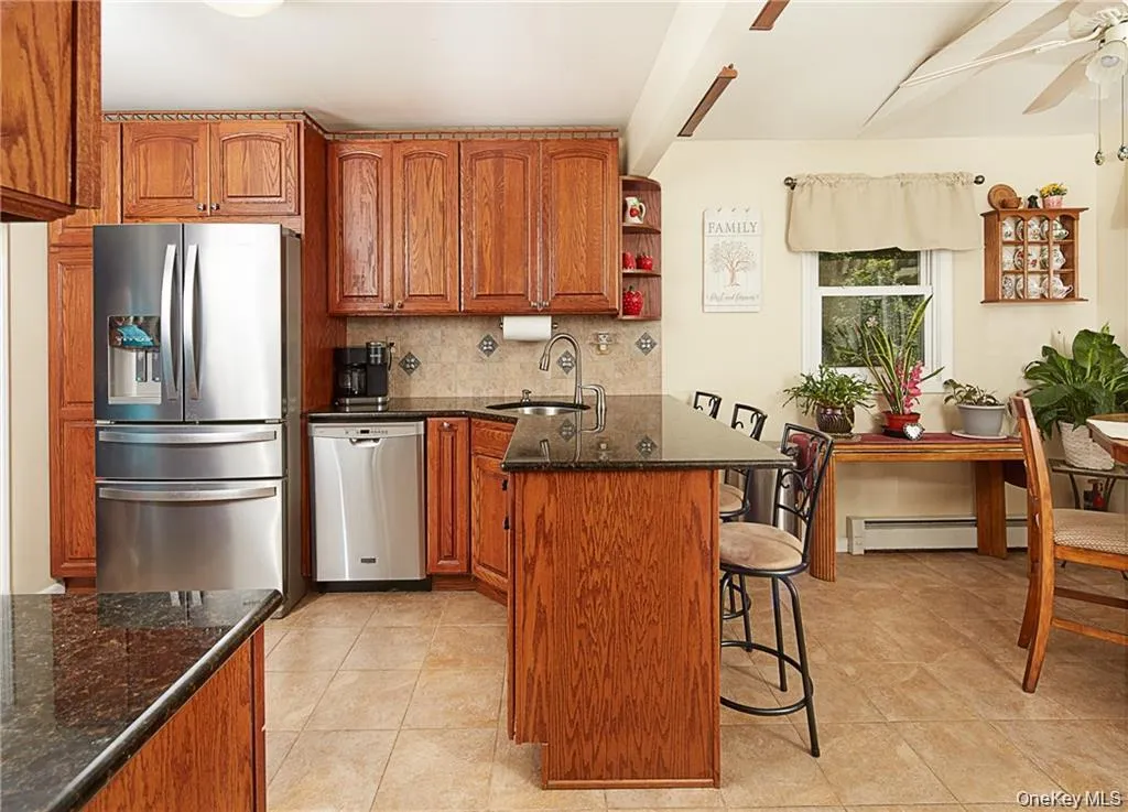 Kitchen featuring brown cabinets, dark stone countertops, stainless steel appliances, decorative backsplash, and a kitchen breakfast bar Kitchen featuring brown cabinets, dark stone countertops, stainless steel appliances, decorative backsplash, and a kitchen breakfast bar