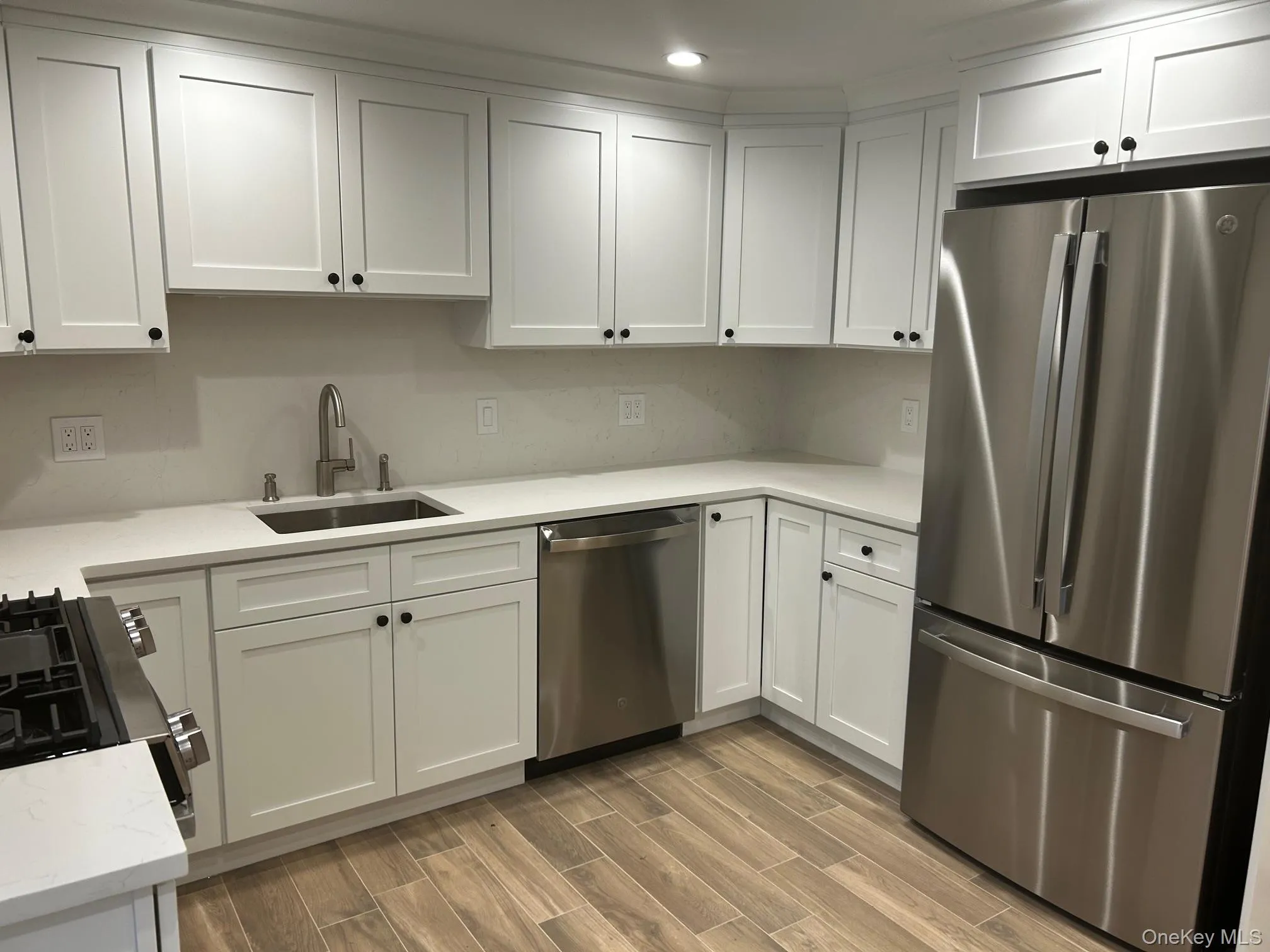 Kitchen with appliances with stainless steel finishes, white cabinets, wood tiled floors, and light stone countertops Kitchen with appliances with stainless steel finishes, white cabinets, wood tiled floors, and light stone countertops