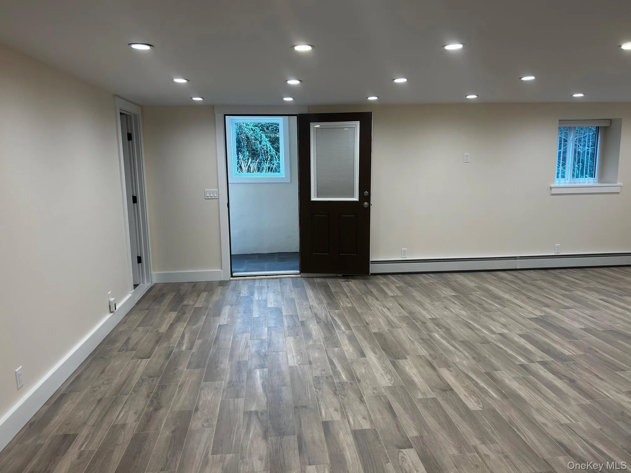 Living room featuring recessed lighting, wood finished floors, and a baseboard heating unit Living room featuring recessed lighting, wood finished floors, and a baseboard heating unit