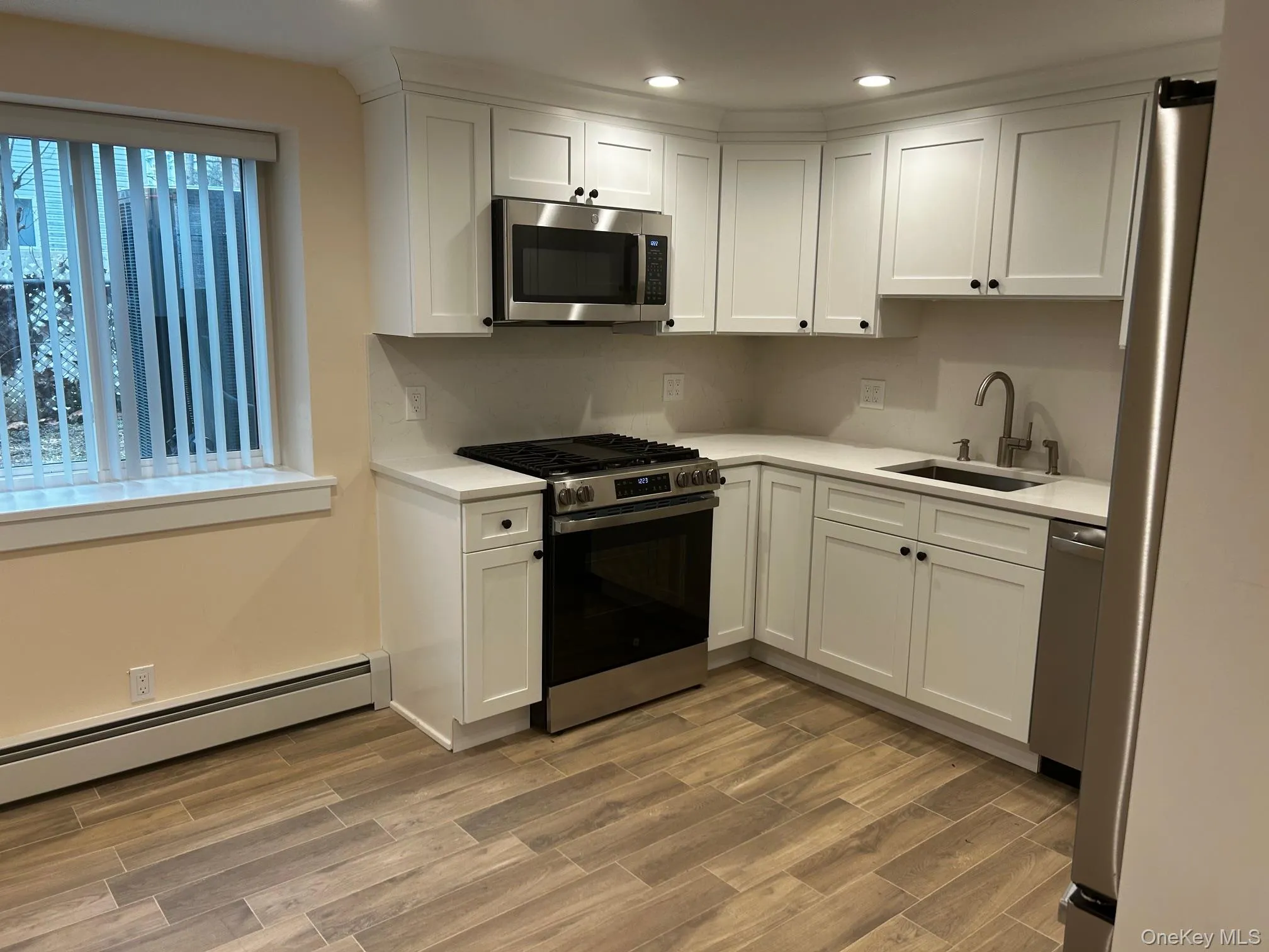 Kitchen with white cabinets, appliances with stainless steel finishes, light wood-style flooring, baseboard heating, and recessed lighting Kitchen with white cabinets, appliances with stainless steel finishes, light wood-style flooring, baseboard heating, and recessed lighting