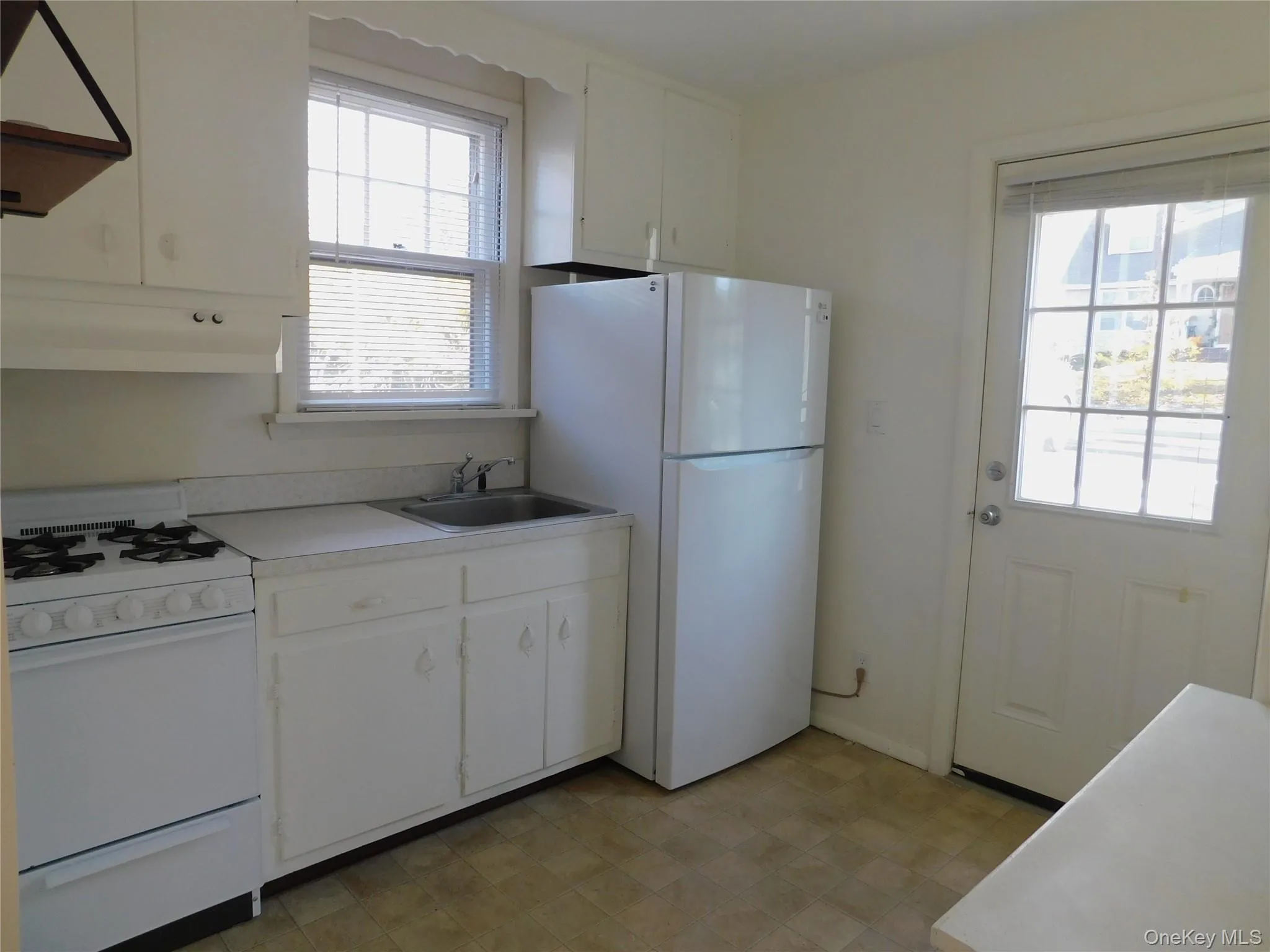 Kitchen featuring white appliances, white cabinetry, extractor fan, light countertops, and under cabinet range hood Kitchen featuring white appliances, white cabinetry, extractor fan, light countertops, and under cabinet range hood