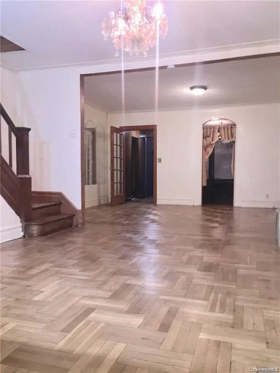 Unfurnished living room featuring arched walkways, stairway, and a chandelier Unfurnished living room featuring arched walkways, stairway, and a chandelier