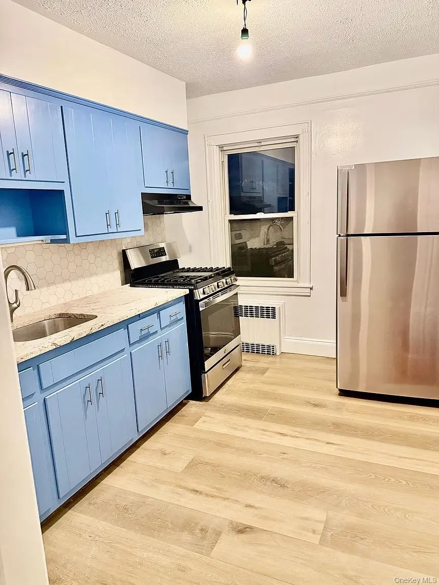 Kitchen featuring blue cabinetry, stainless steel appliances, light stone countertops, a textured ceiling, and backsplash Kitchen featuring blue cabinetry, stainless steel appliances, light stone countertops, a textured ceiling, and backsplash