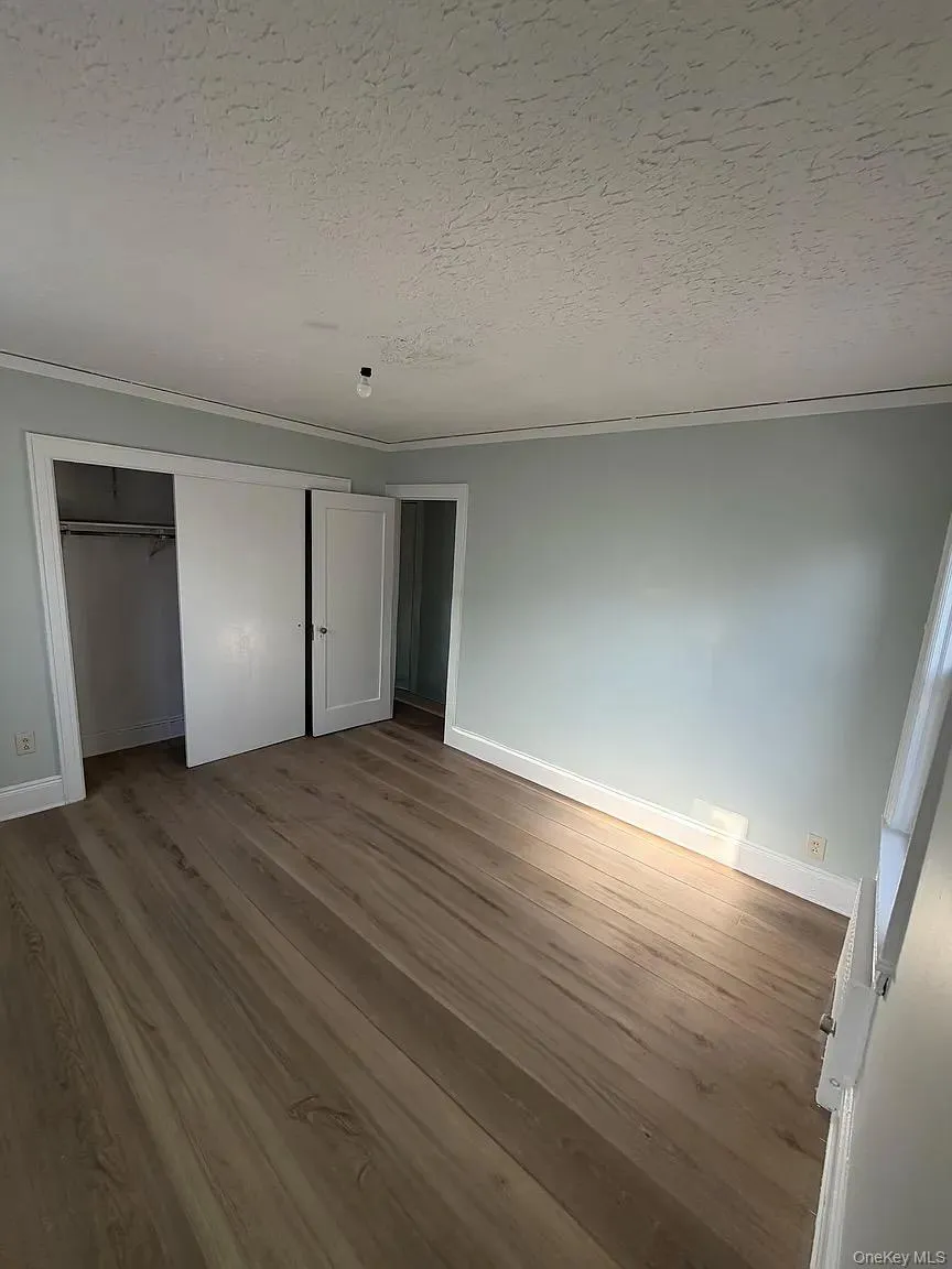 Unfurnished bedroom with a textured ceiling, wood finished floors, a closet, and crown molding Unfurnished bedroom with a textured ceiling, wood finished floors, a closet, and crown molding