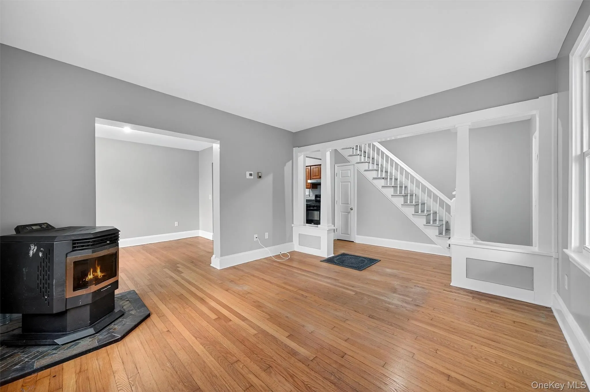 Unfurnished living room featuring a wood stove, light wood finished floors, and stairway Unfurnished living room featuring a wood stove, light wood finished floors, and stairway