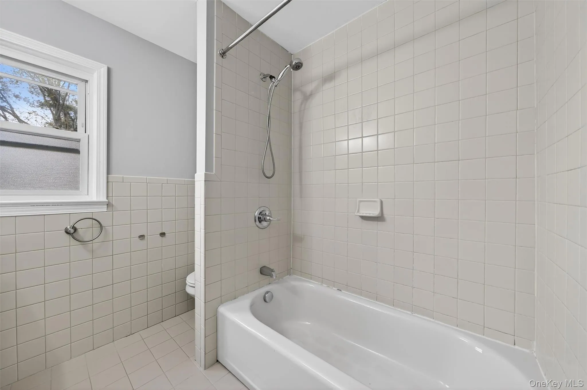 Bathroom featuring shower / tub combination, tile patterned floors, tile walls, and wainscoting Bathroom featuring shower / tub combination, tile patterned floors, tile walls, and wainscoting