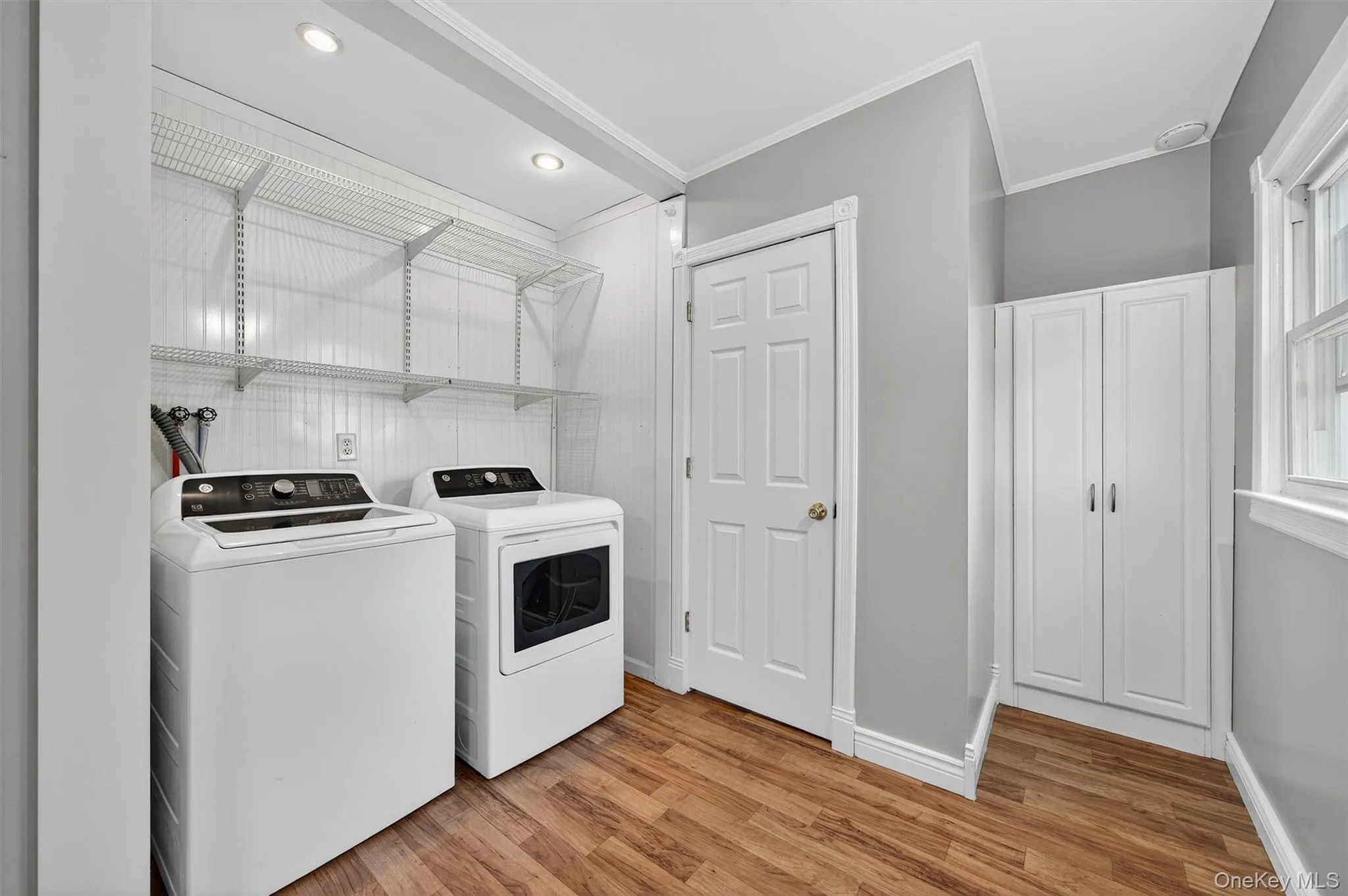 Washroom with crown molding, light wood-style floors, and washing machine and dryer Washroom with crown molding, light wood-style floors, and washing machine and dryer