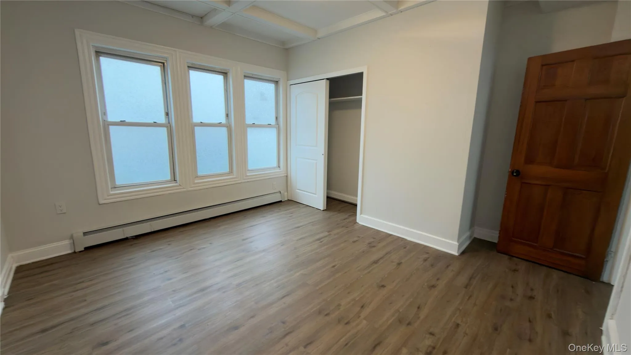 Unfurnished bedroom featuring a baseboard heating unit, light wood-style floors, coffered ceiling, a closet, and beam ceiling Unfurnished bedroom featuring a baseboard heating unit, light wood-style floors, coffered ceiling, a closet, and beam ceiling