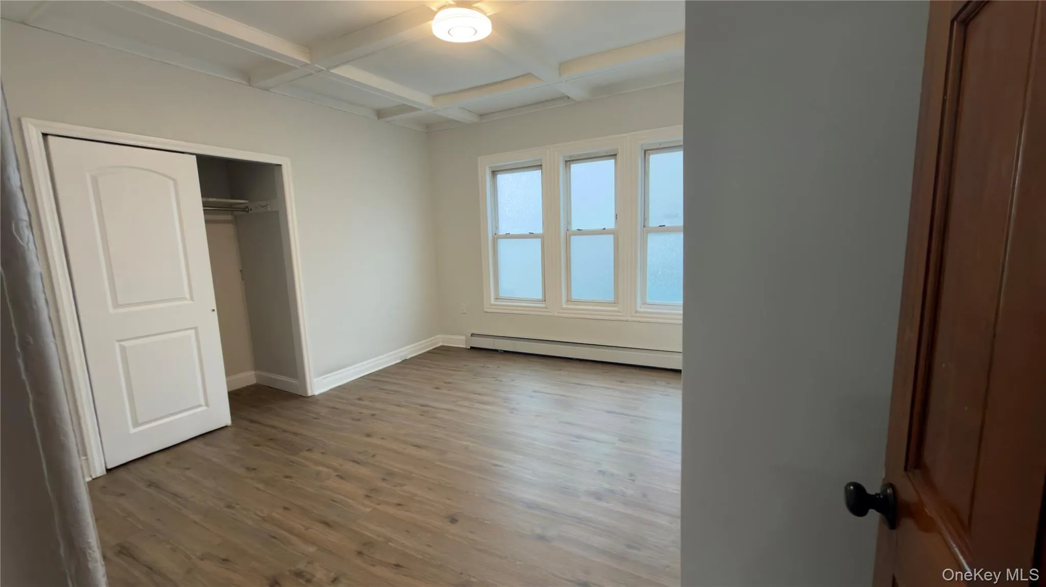Unfurnished bedroom with coffered ceiling, beamed ceiling, a closet, wood finished floors, and a baseboard radiator Unfurnished bedroom with coffered ceiling, beamed ceiling, a closet, wood finished floors, and a baseboard radiator