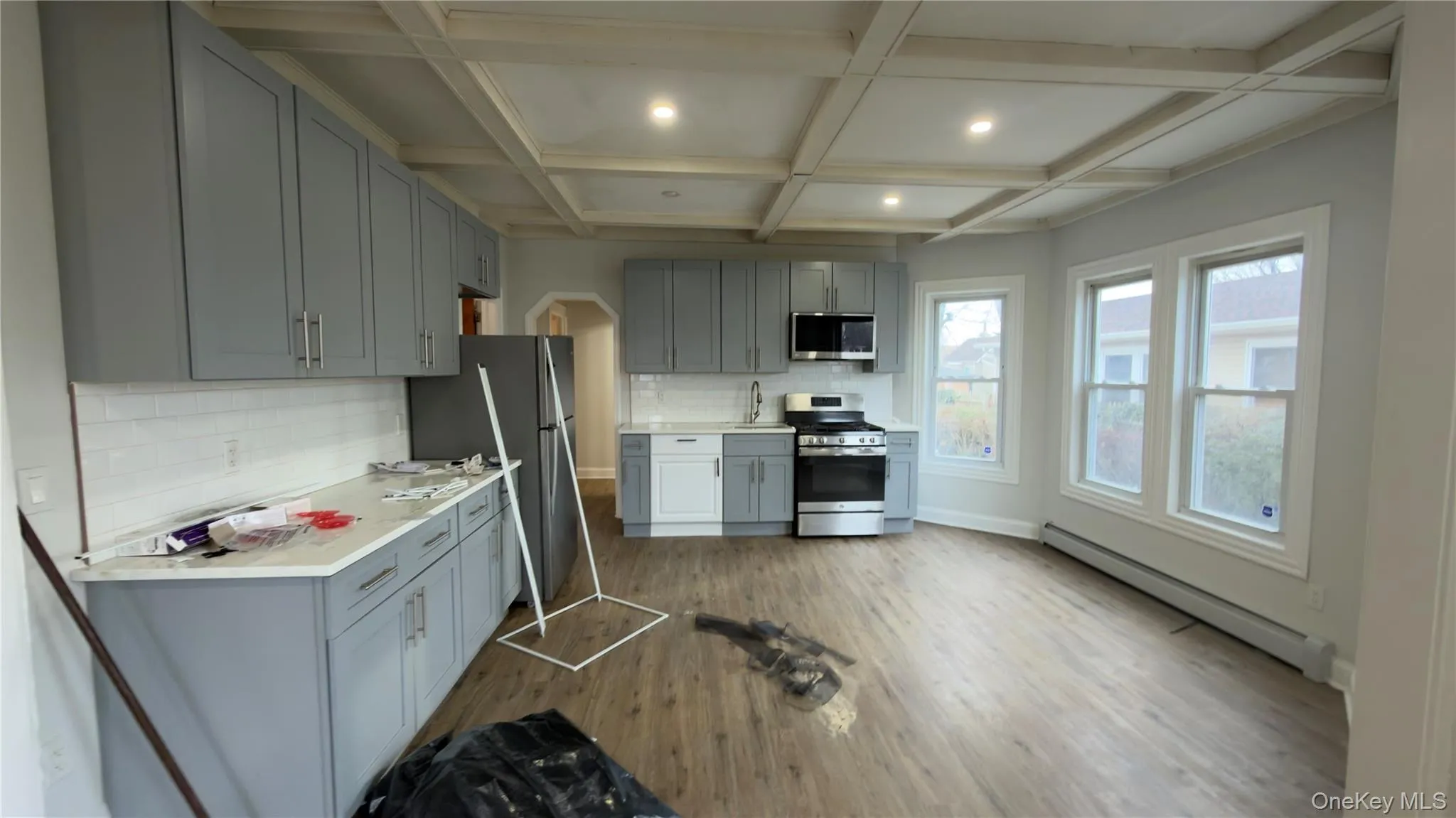 Kitchen featuring gray cabinetry, backsplash, a baseboard heating unit, appliances with stainless steel finishes, and coffered ceiling Kitchen featuring gray cabinetry, backsplash, a baseboard heating unit, appliances with stainless steel finishes, and coffered ceiling