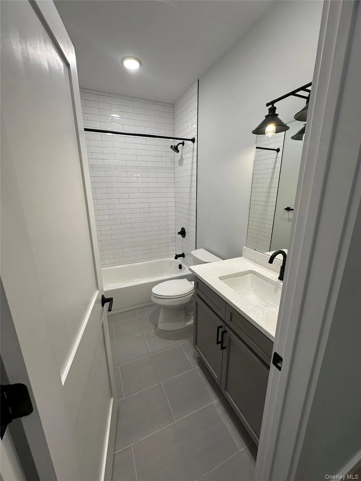 Full bathroom with tile patterned floors, vanity, toilet, and tiled shower / bath combo Full bathroom with tile patterned floors, vanity, toilet, and tiled shower / bath combo