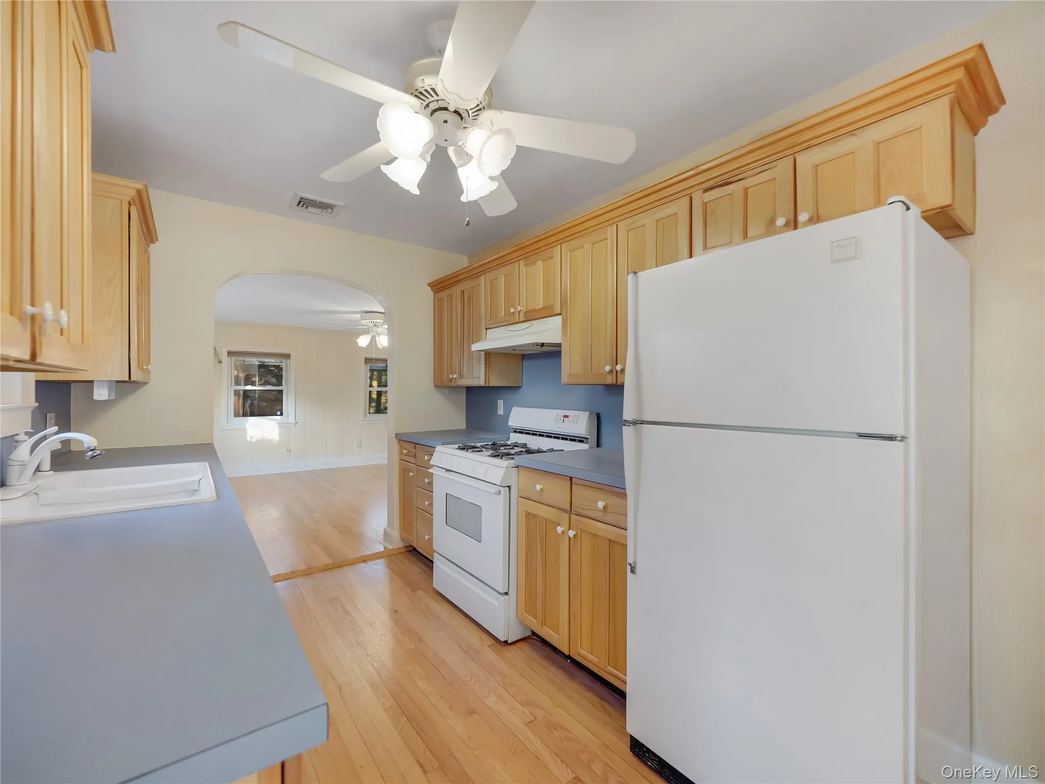 Kitchen with white appliances, light brown cabinetry, and arched walkways Kitchen with white appliances, light brown cabinetry, and arched walkways