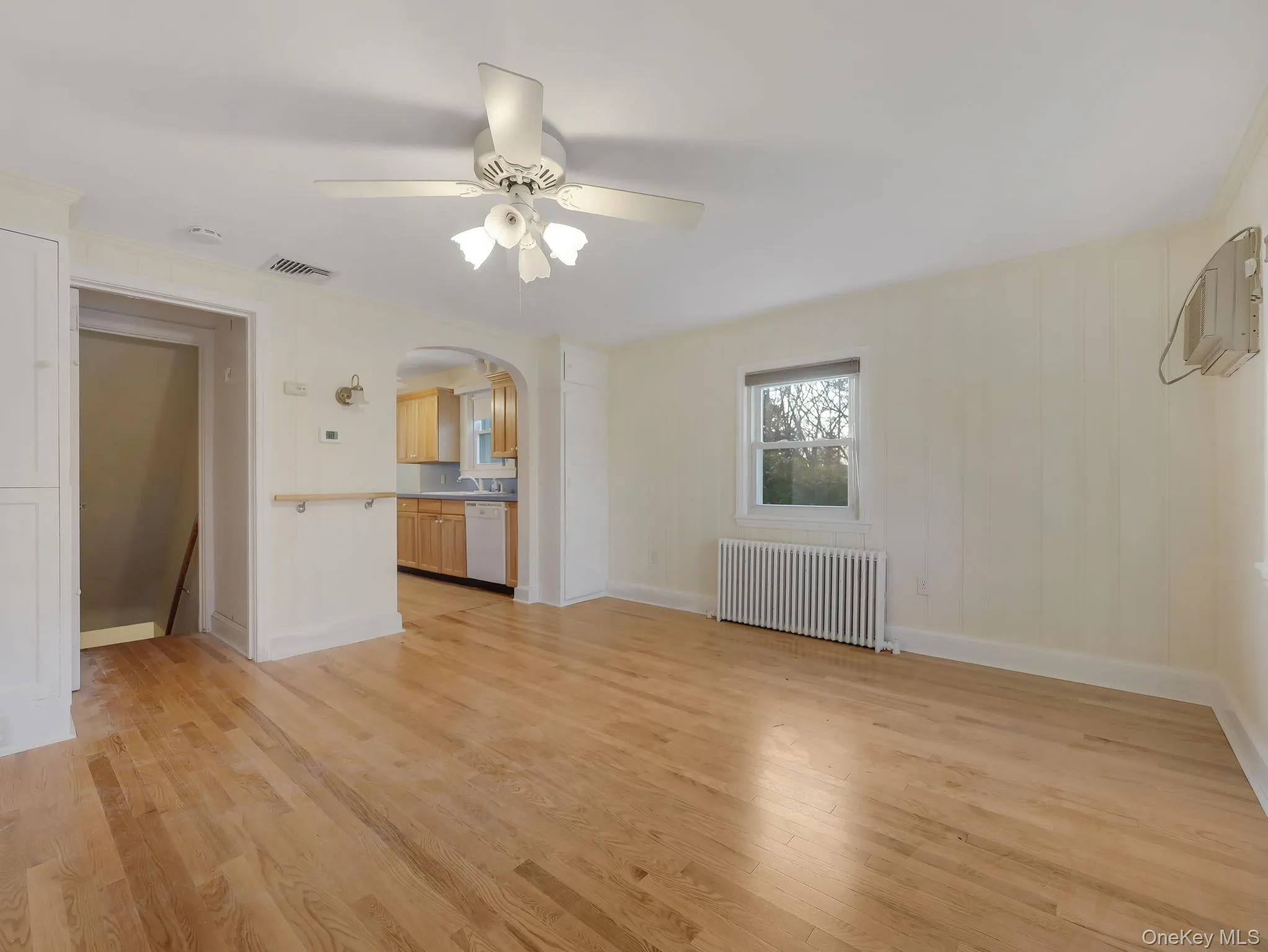 Unfurnished living room featuring arched walkways, radiator heating unit, light wood-style floors, and ceiling fan Unfurnished living room featuring arched walkways, radiator heating unit, light wood-style floors, and ceiling fan