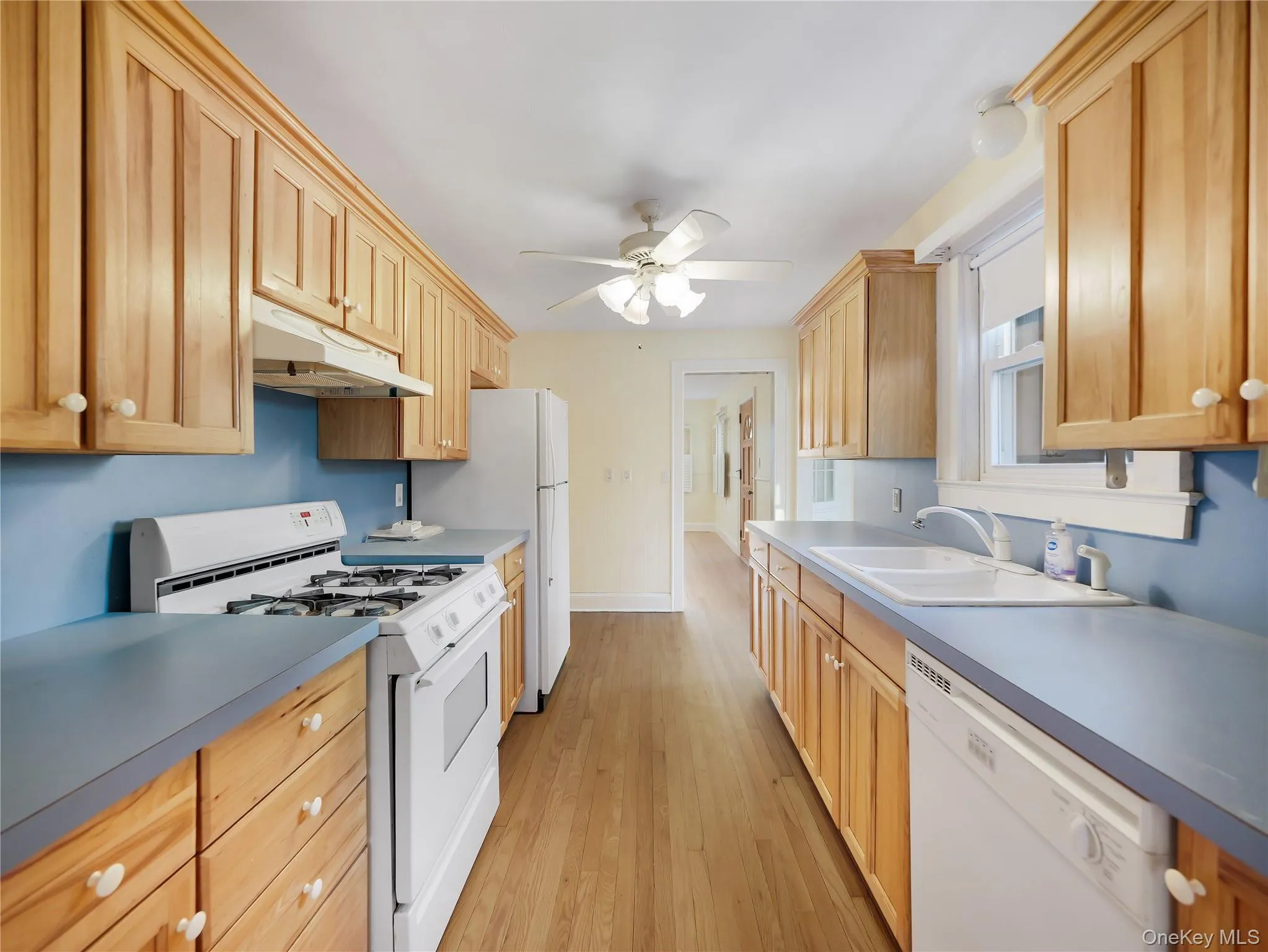 Kitchen with white appliances, under cabinet range hood, light wood-style flooring, and a ceiling fan Kitchen with white appliances, under cabinet range hood, light wood-style flooring, and a ceiling fan