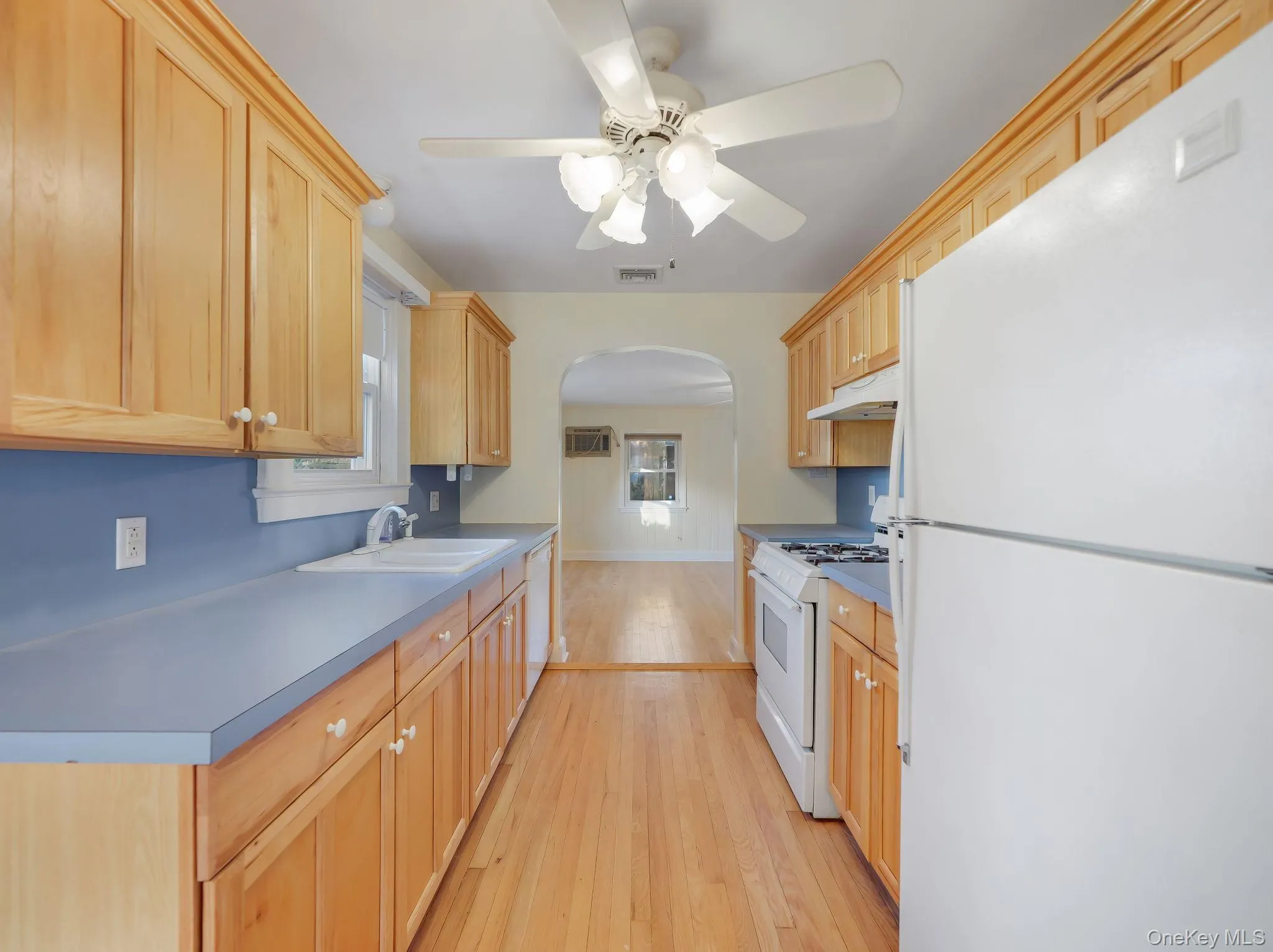 Kitchen with white appliances, arched walkways, light wood finished floors, ceiling fan, and light brown cabinets Kitchen with white appliances, arched walkways, light wood finished floors, ceiling fan, and light brown cabinets