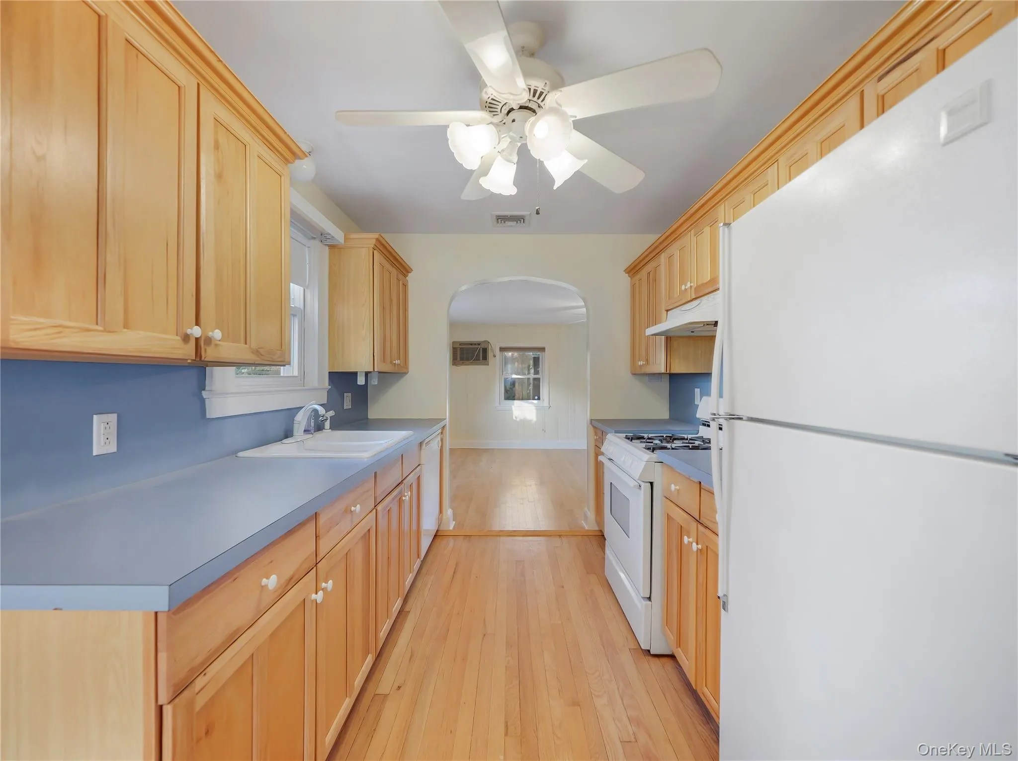Kitchen featuring white appliances, arched walkways, light wood finished floors, a ceiling fan, and light brown cabinetry Kitchen featuring white appliances, arched walkways, light wood finished floors, a ceiling fan, and light brown cabinetry