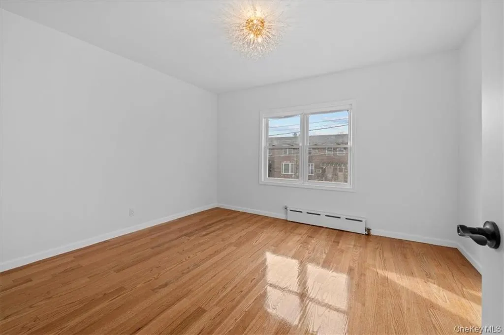 Unfurnished room featuring baseboard heating, light wood-style flooring, and a chandelier Unfurnished room featuring baseboard heating, light wood-style flooring, and a chandelier