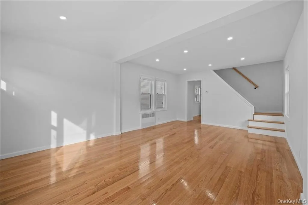 Unfurnished living room featuring light wood-style floors, stairway, recessed lighting, and radiator Unfurnished living room featuring light wood-style floors, stairway, recessed lighting, and radiator