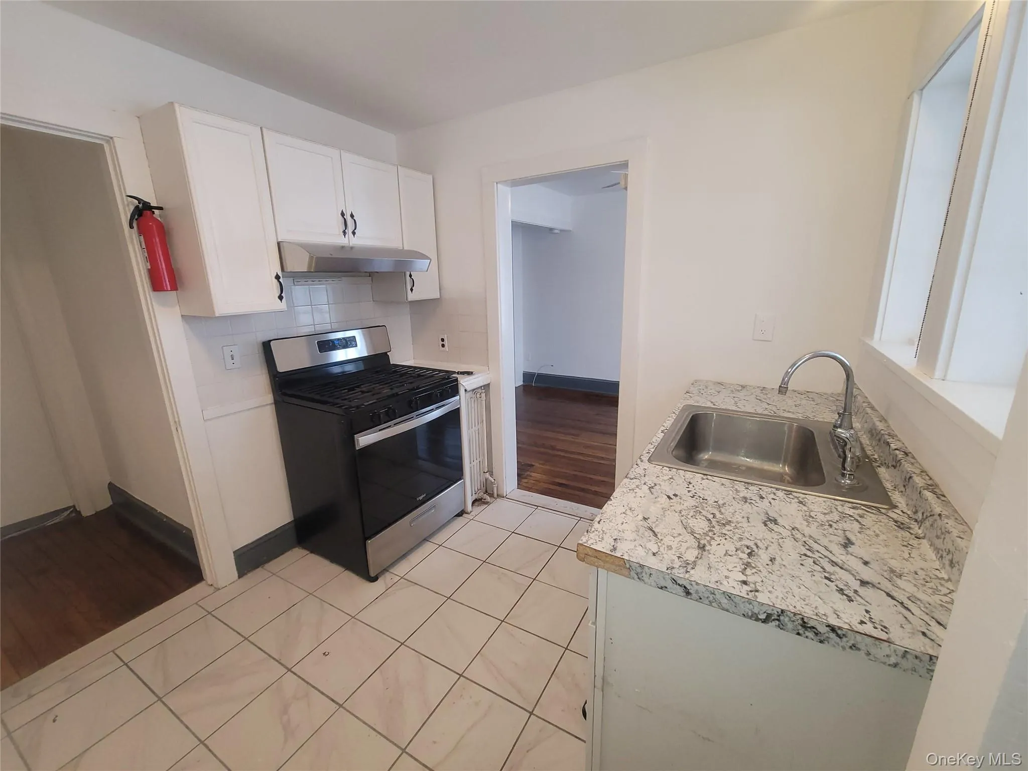 Kitchen with stainless steel range with gas stovetop, white cabinets, light countertops, light tile patterned floors, and tasteful backsplash Kitchen with stainless steel range with gas stovetop, white cabinets, light countertops, light tile patterned floors, and tasteful backsplash