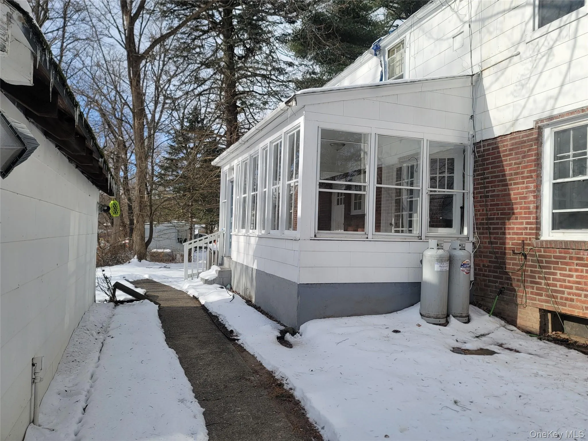 View of snowy exterior featuring a sunroom and brick siding View of snowy exterior featuring a sunroom and brick siding