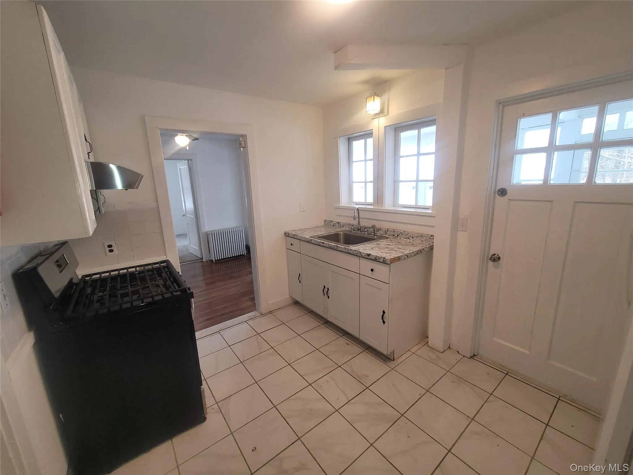 Kitchen featuring white cabinetry, gas stove, radiator heating unit, range hood, and light tile patterned floors Kitchen featuring white cabinetry, gas stove, radiator heating unit, range hood, and light tile patterned floors