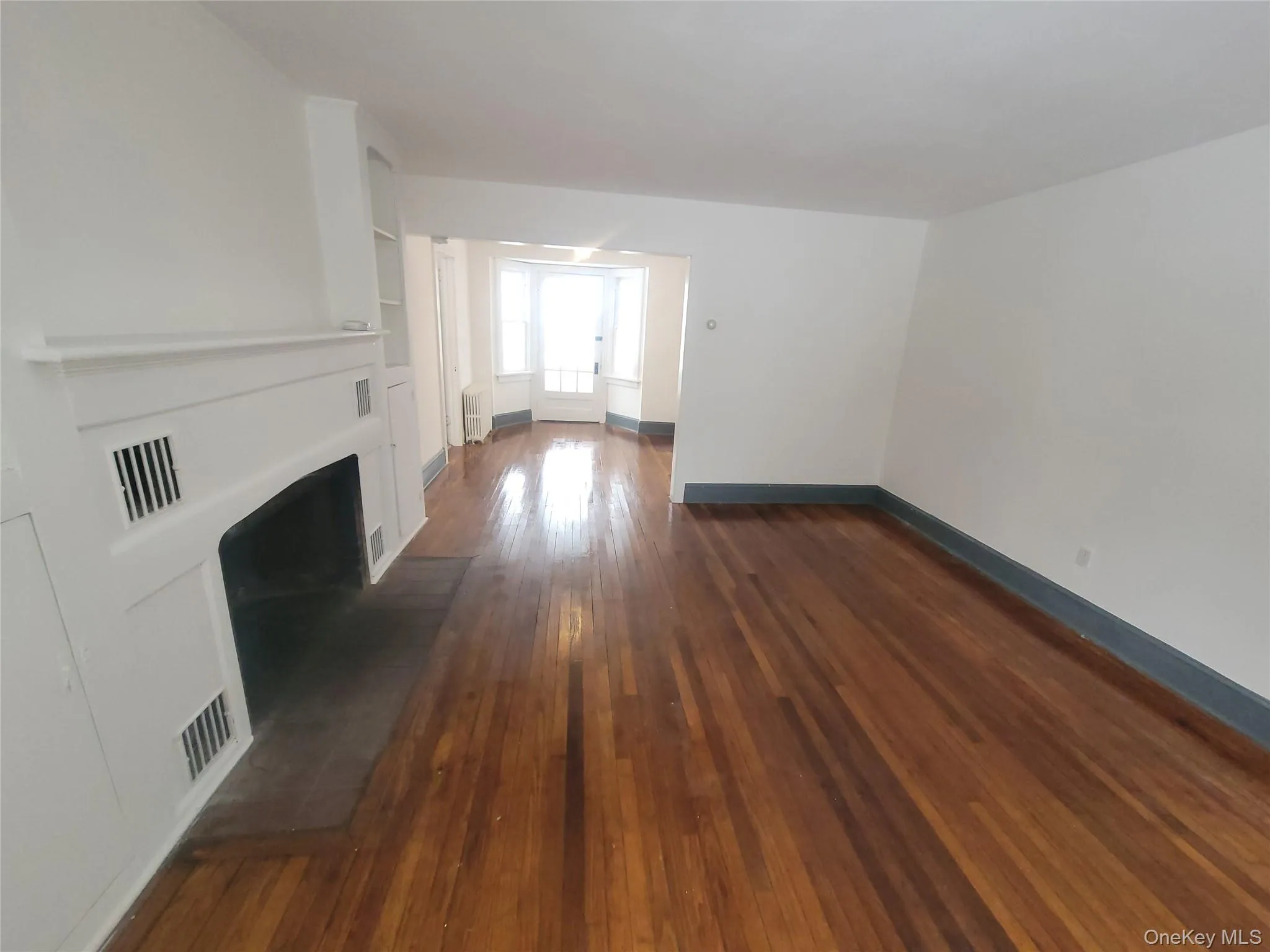 Unfurnished living room with dark wood-style flooring, a fireplace with flush hearth, and radiator heating unit Unfurnished living room with dark wood-style flooring, a fireplace with flush hearth, and radiator heating unit