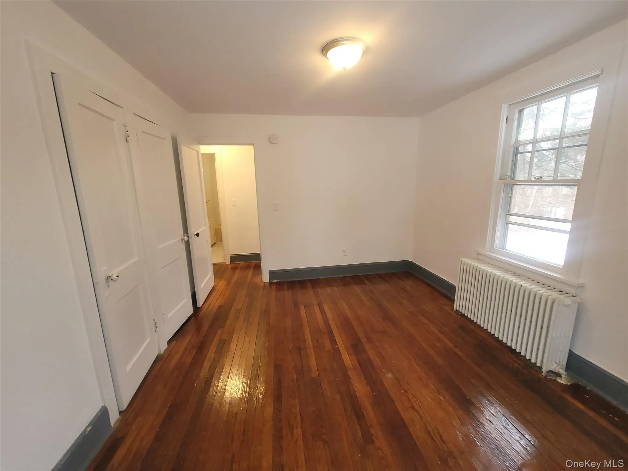 Unfurnished bedroom featuring radiator heating unit, dark wood-style flooring, and a closet Unfurnished bedroom featuring radiator heating unit, dark wood-style flooring, and a closet