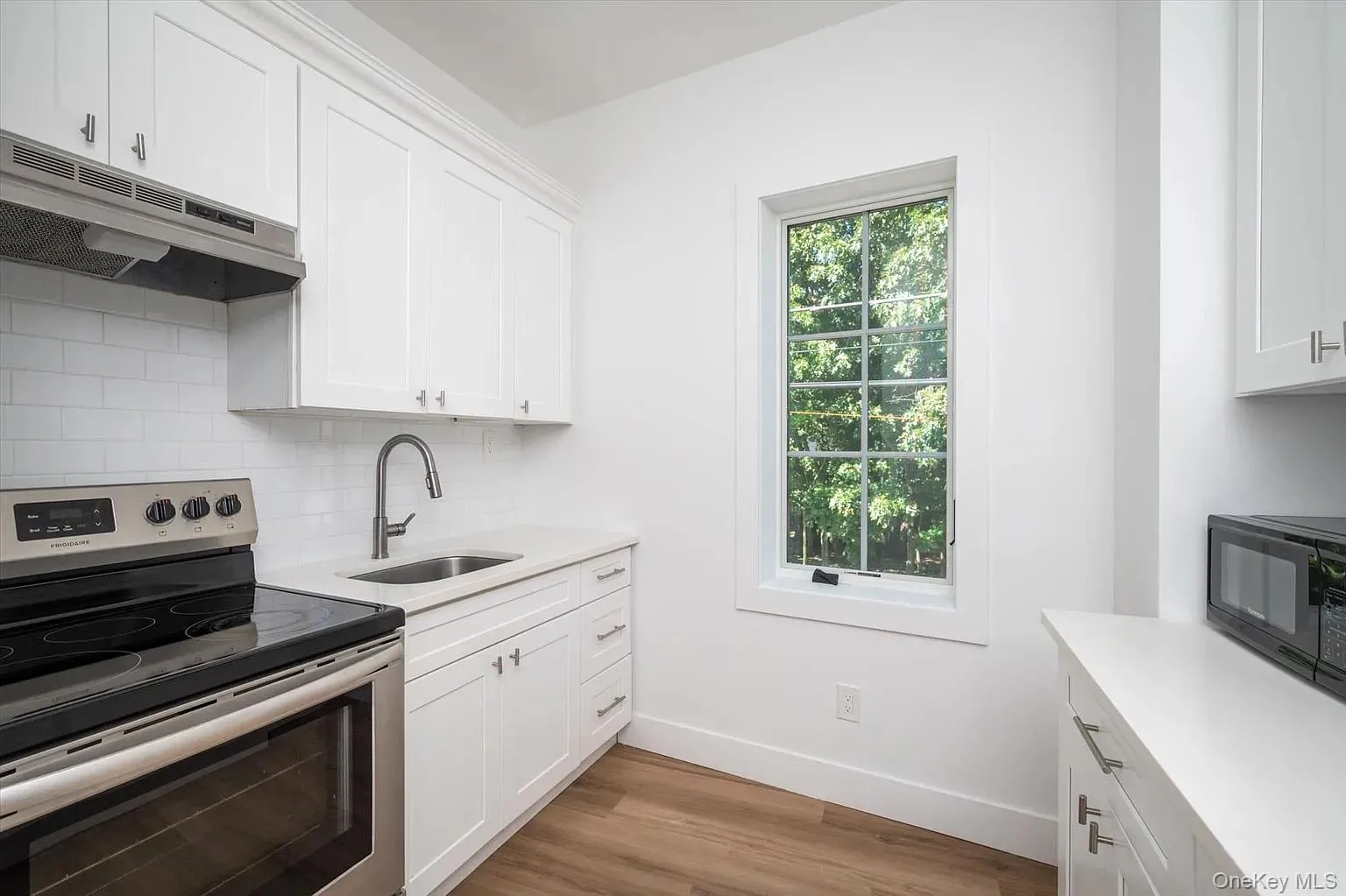 Kitchen featuring stainless steel range with electric cooktop, white cabinets, under cabinet range hood, black microwave, and tasteful backsplash Kitchen featuring stainless steel range with electric cooktop, white cabinets, under cabinet range hood, black microwave, and tasteful backsplash