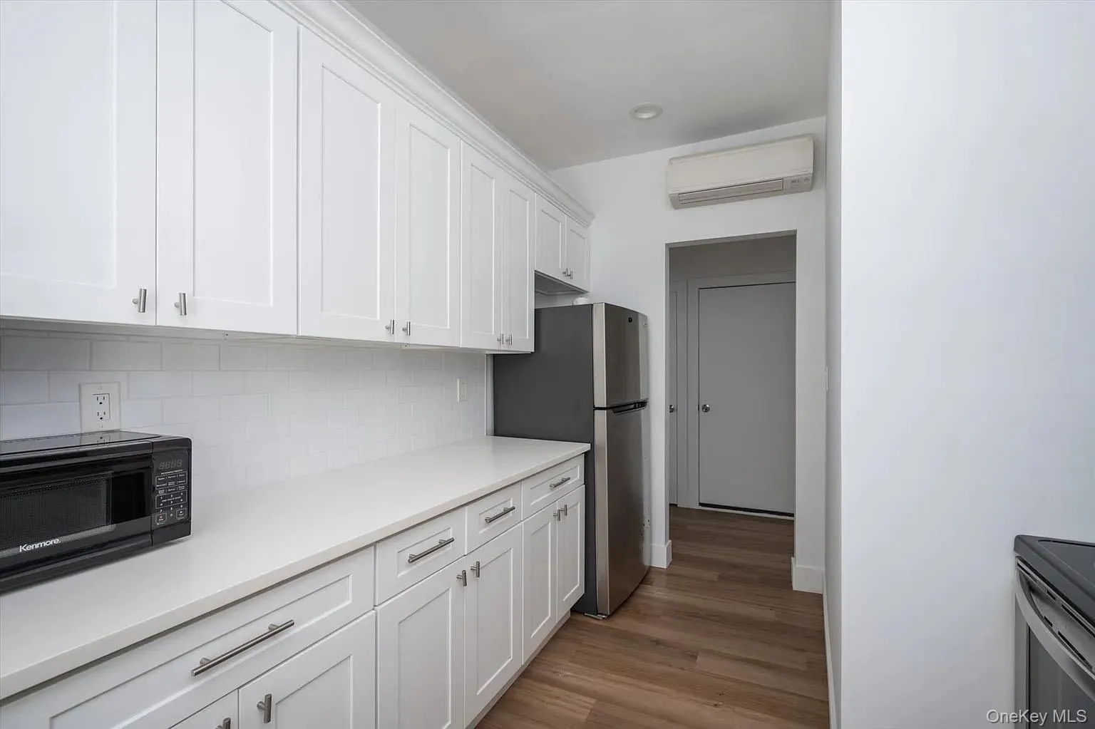 Kitchen featuring white cabinets, a wall mounted AC, light wood-style flooring, freestanding refrigerator, and tasteful backsplash Kitchen featuring white cabinets, a wall mounted AC, light wood-style flooring, freestanding refrigerator, and tasteful backsplash