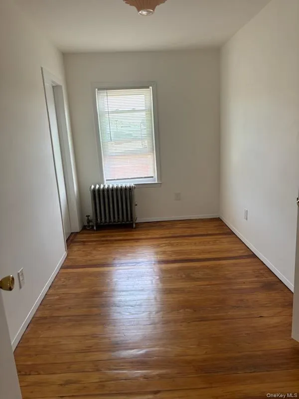 Unfurnished room with radiator heating unit and dark wood finished floors Unfurnished room with radiator heating unit and dark wood finished floors