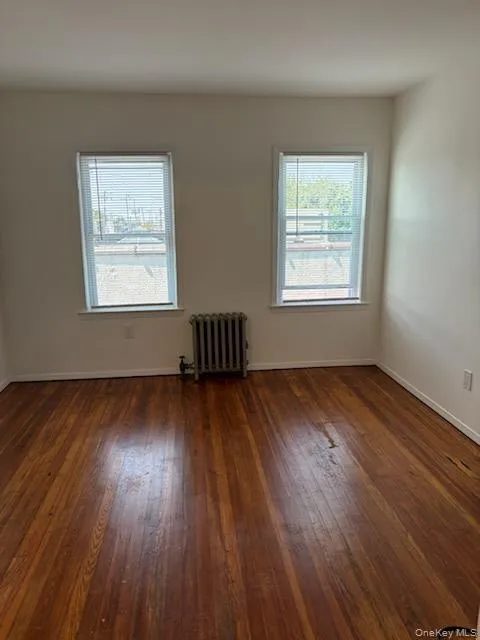 Spare room with dark wood-type flooring, radiator heating unit, and healthy amount of natural light Spare room with dark wood-type flooring, radiator heating unit, and healthy amount of natural light