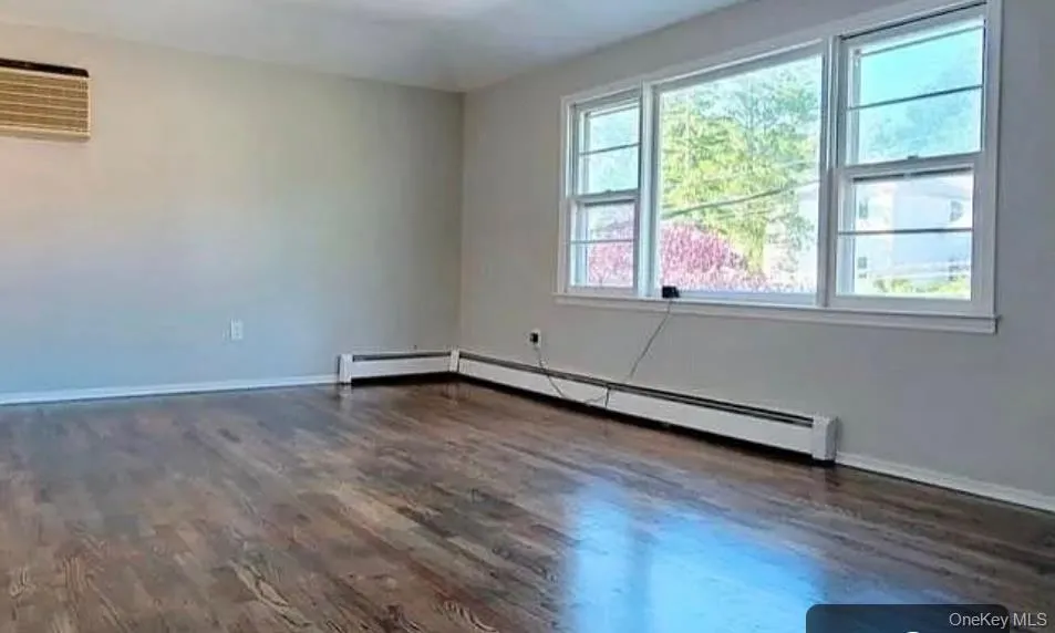 Empty room featuring dark wood finished floors and baseboard heating Empty room featuring dark wood finished floors and baseboard heating