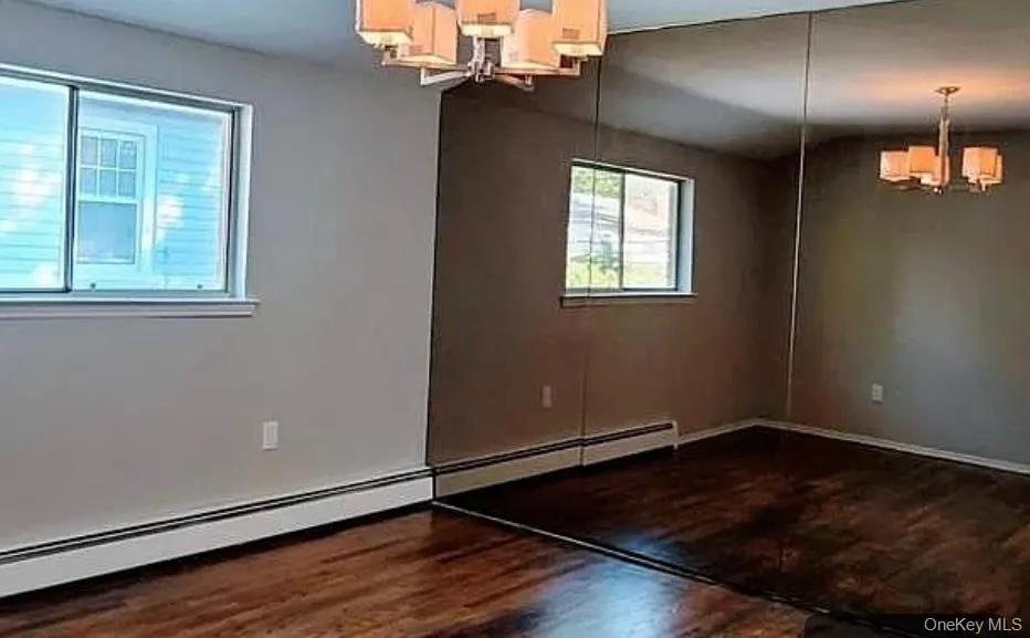 Unfurnished dining area featuring a chandelier, a baseboard heating unit, and dark wood finished floors Unfurnished dining area featuring a chandelier, a baseboard heating unit, and dark wood finished floors