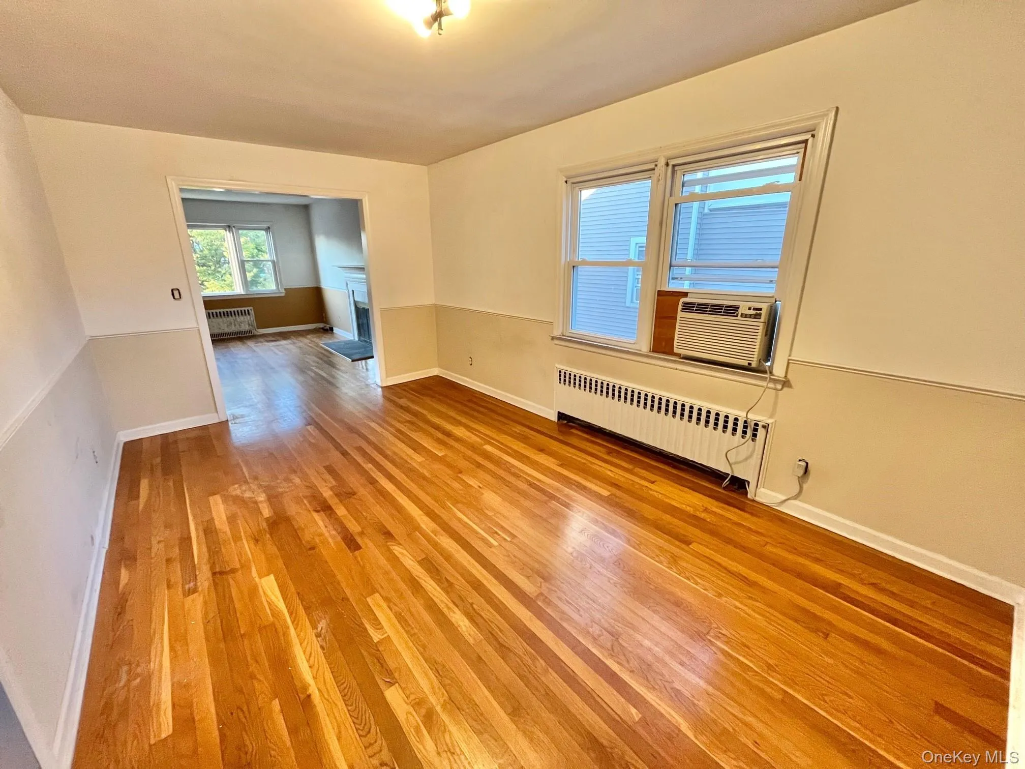 Unfurnished room featuring light wood-type flooring, radiator, a fireplace, and cooling unit Unfurnished room featuring light wood-type flooring, radiator, a fireplace, and cooling unit