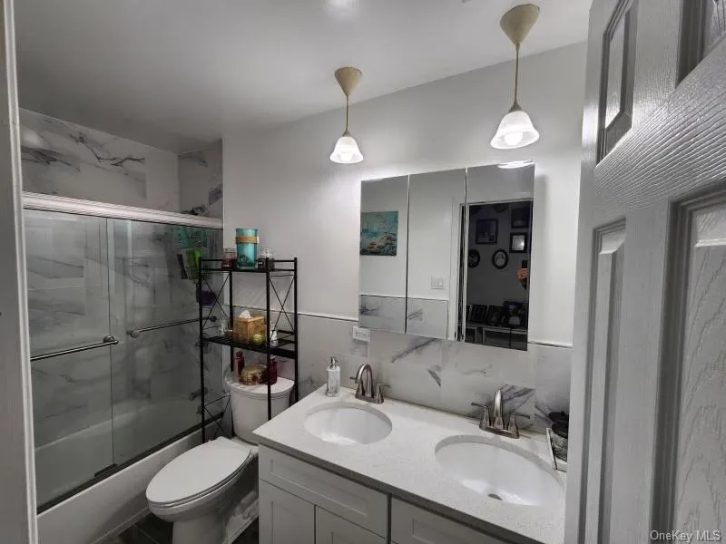 Full bathroom with double vanity, bath / shower combo with glass door, and tasteful backsplash Full bathroom with double vanity, bath / shower combo with glass door, and tasteful backsplash