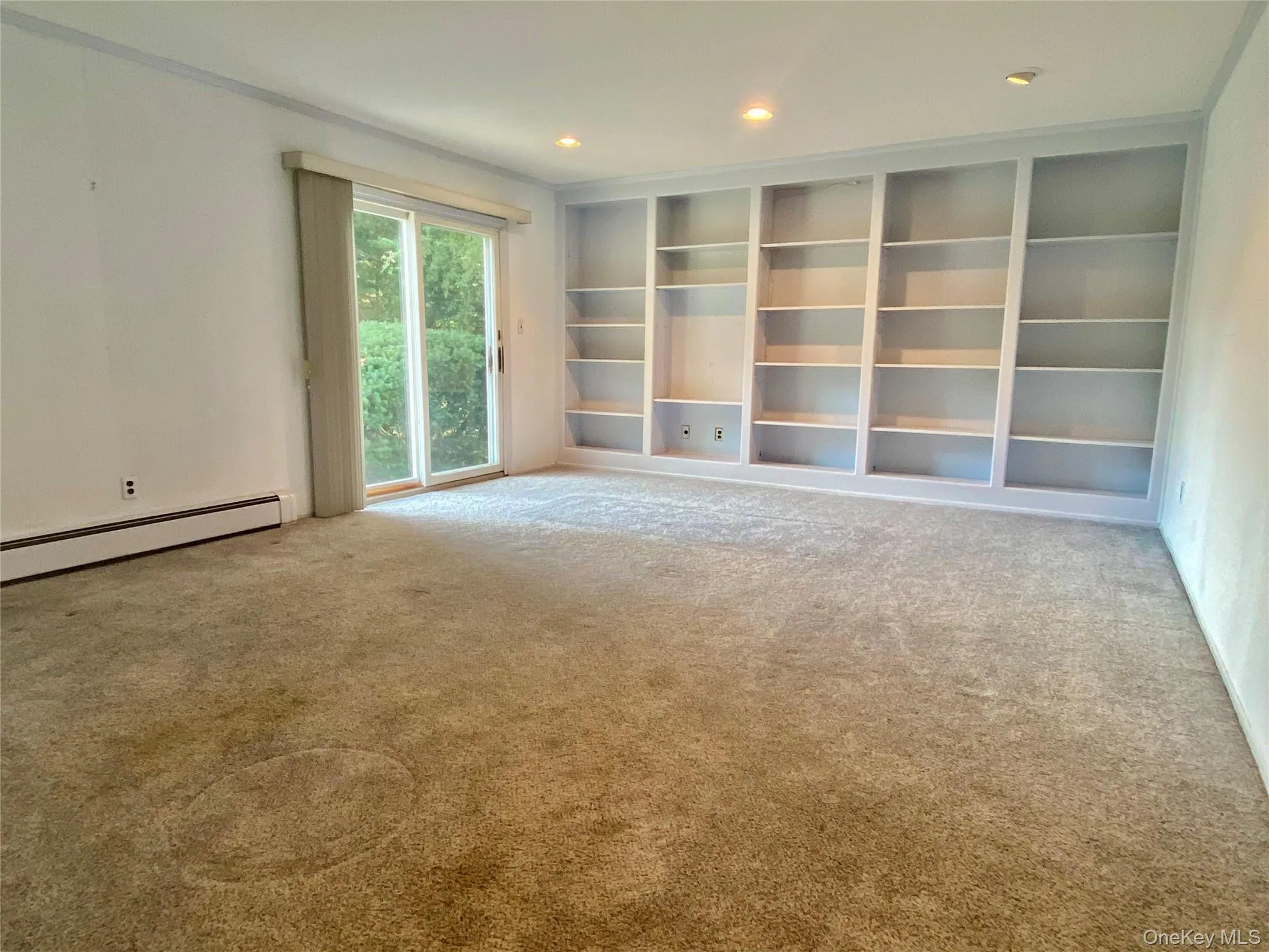 Unfurnished living room featuring light carpet, recessed lighting, baseboard heating, and built in shelves Unfurnished living room featuring light carpet, recessed lighting, baseboard heating, and built in shelves