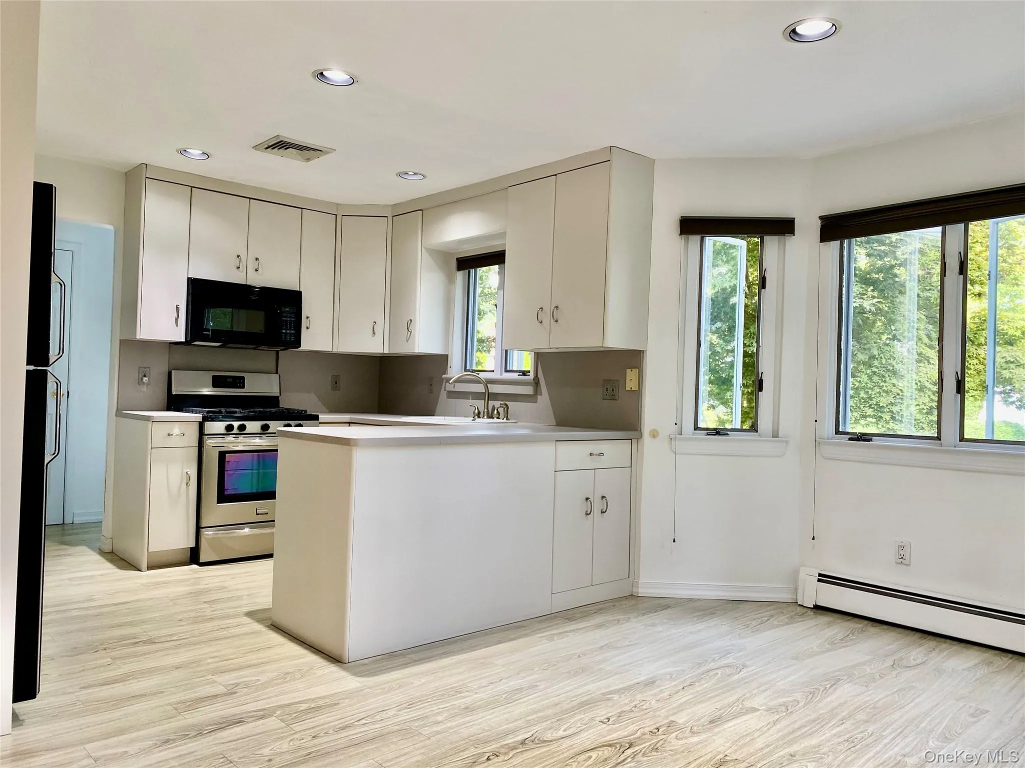 Kitchen featuring black appliances, a peninsula, light countertops, light wood-style flooring, and recessed lighting Kitchen featuring black appliances, a peninsula, light countertops, light wood-style flooring, and recessed lighting