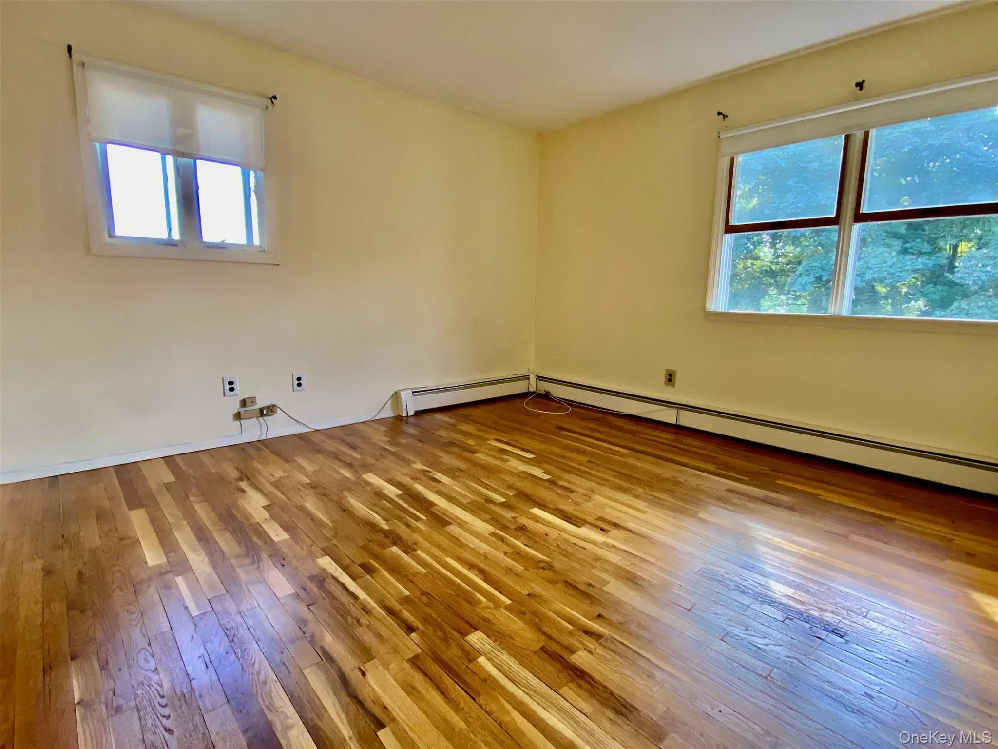 Empty room with light wood-type flooring and a baseboard heating unit Empty room with light wood-type flooring and a baseboard heating unit