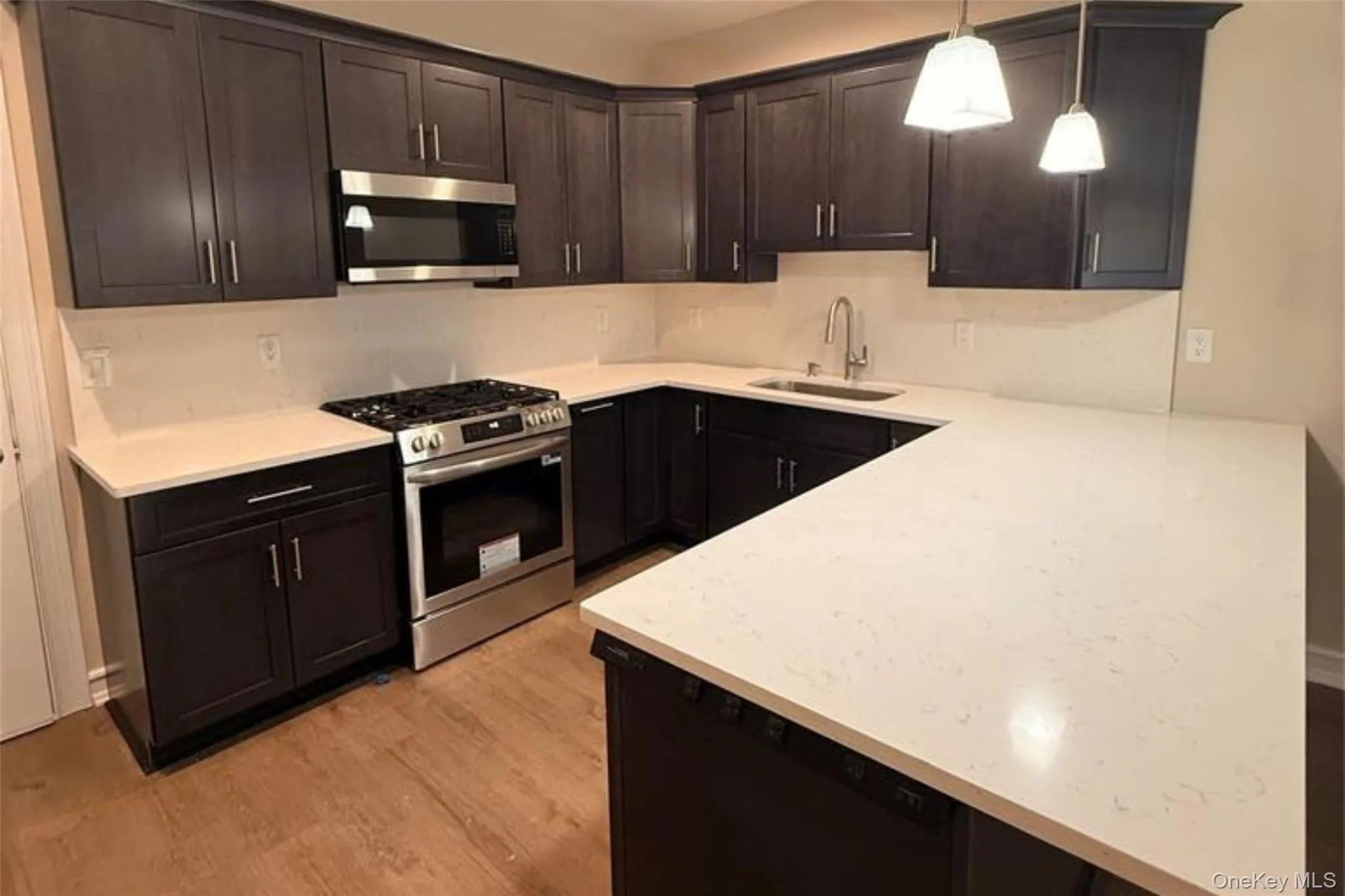 Kitchen featuring appliances with stainless steel finishes, dark brown cabinets, pendant lighting, light stone countertops, and a peninsula Kitchen featuring appliances with stainless steel finishes, dark brown cabinets, pendant lighting, light stone countertops, and a peninsula