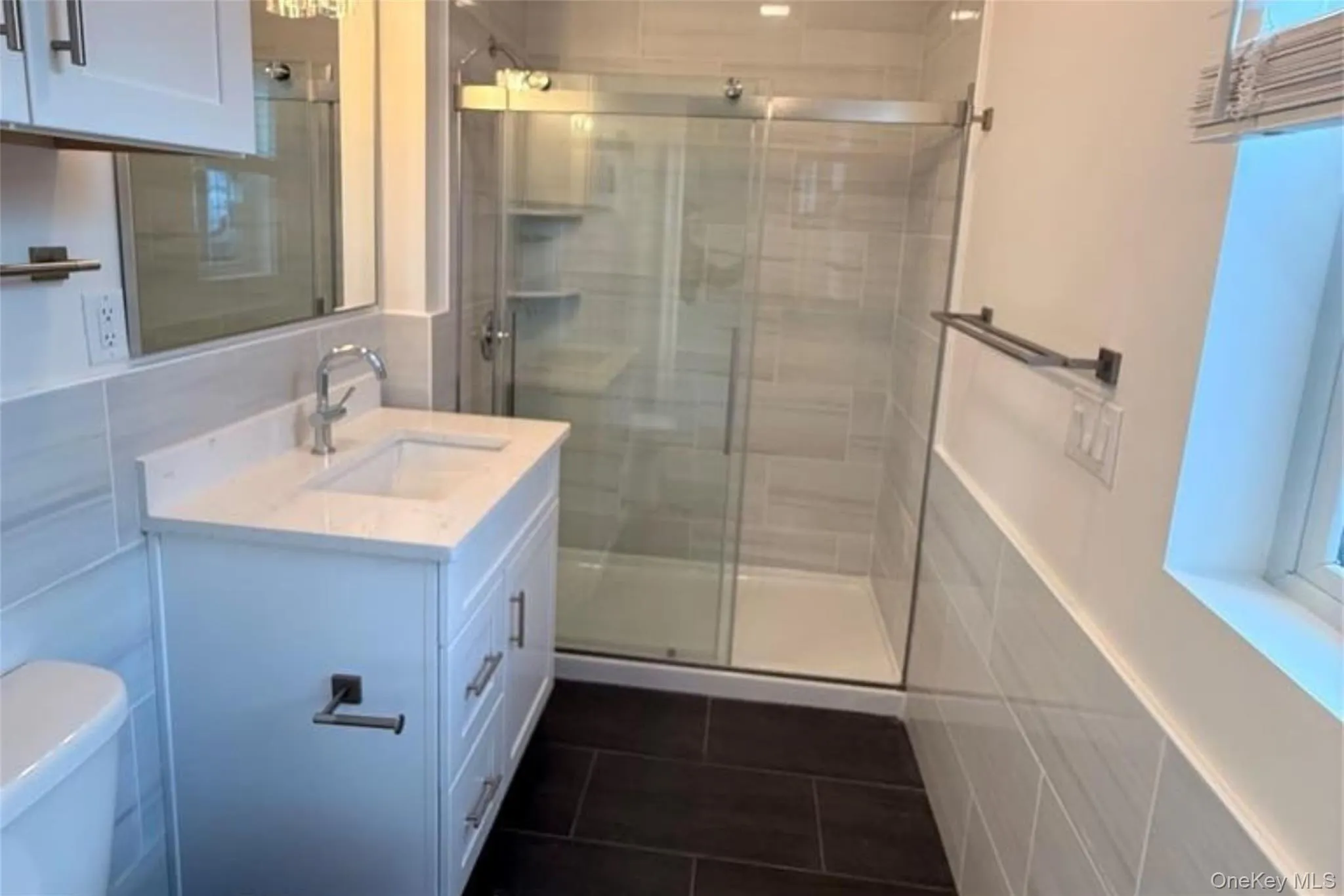 Full bath featuring vanity, a stall shower, dark tile patterned floors, and tile walls Full bath featuring vanity, a stall shower, dark tile patterned floors, and tile walls
