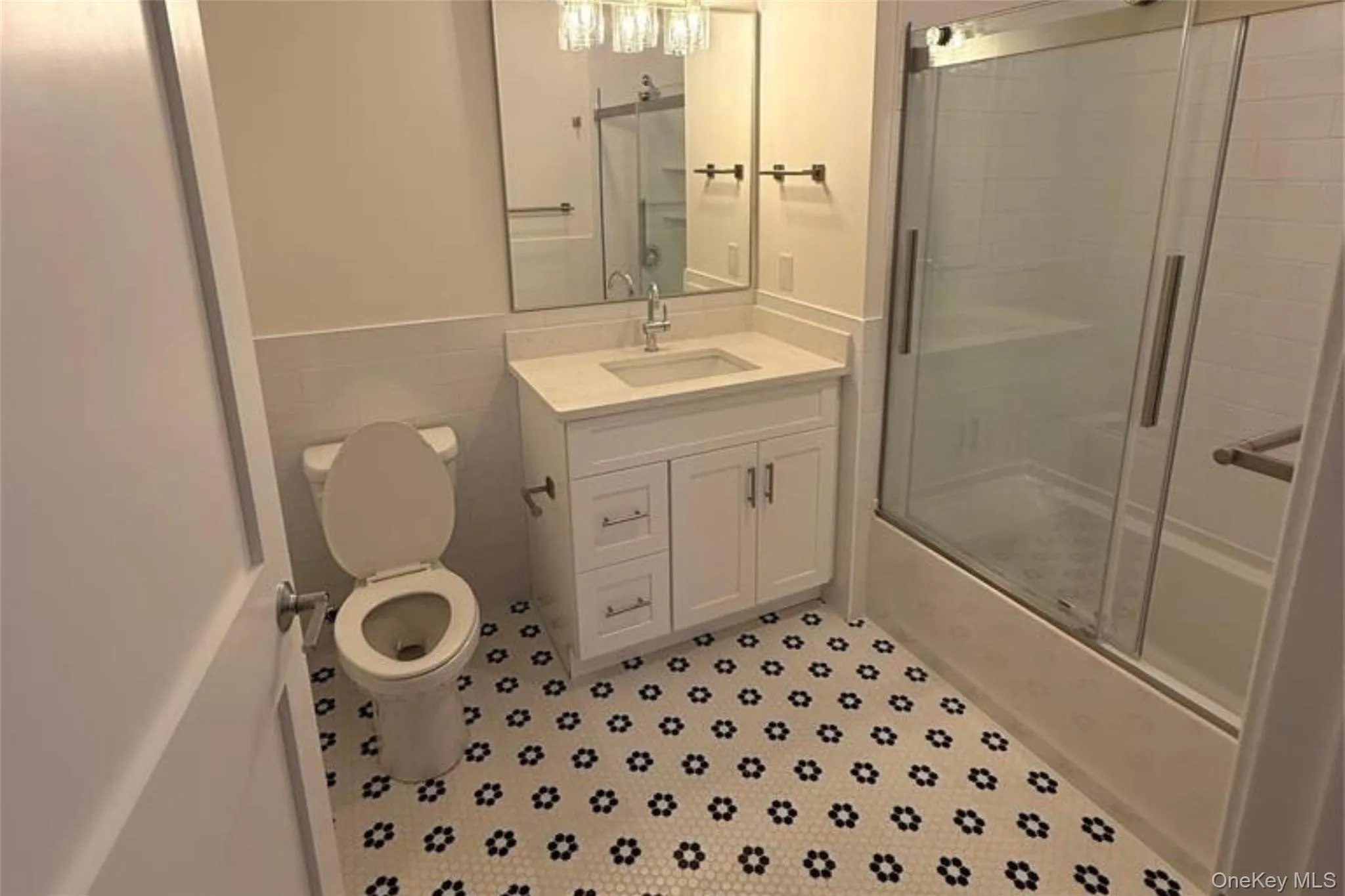 Bathroom with vanity, tile walls, shower / bath combination with glass door, and a wainscoted wall Bathroom with vanity, tile walls, shower / bath combination with glass door, and a wainscoted wall