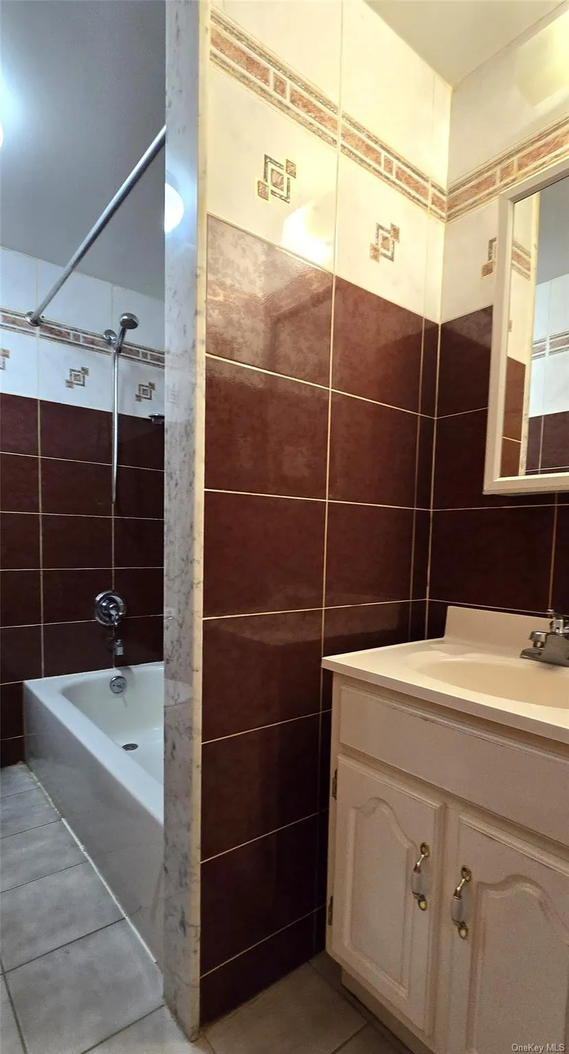 Bathroom featuring light tile patterned flooring, tile walls, vanity, and washtub / shower combination Bathroom featuring light tile patterned flooring, tile walls, vanity, and washtub / shower combination