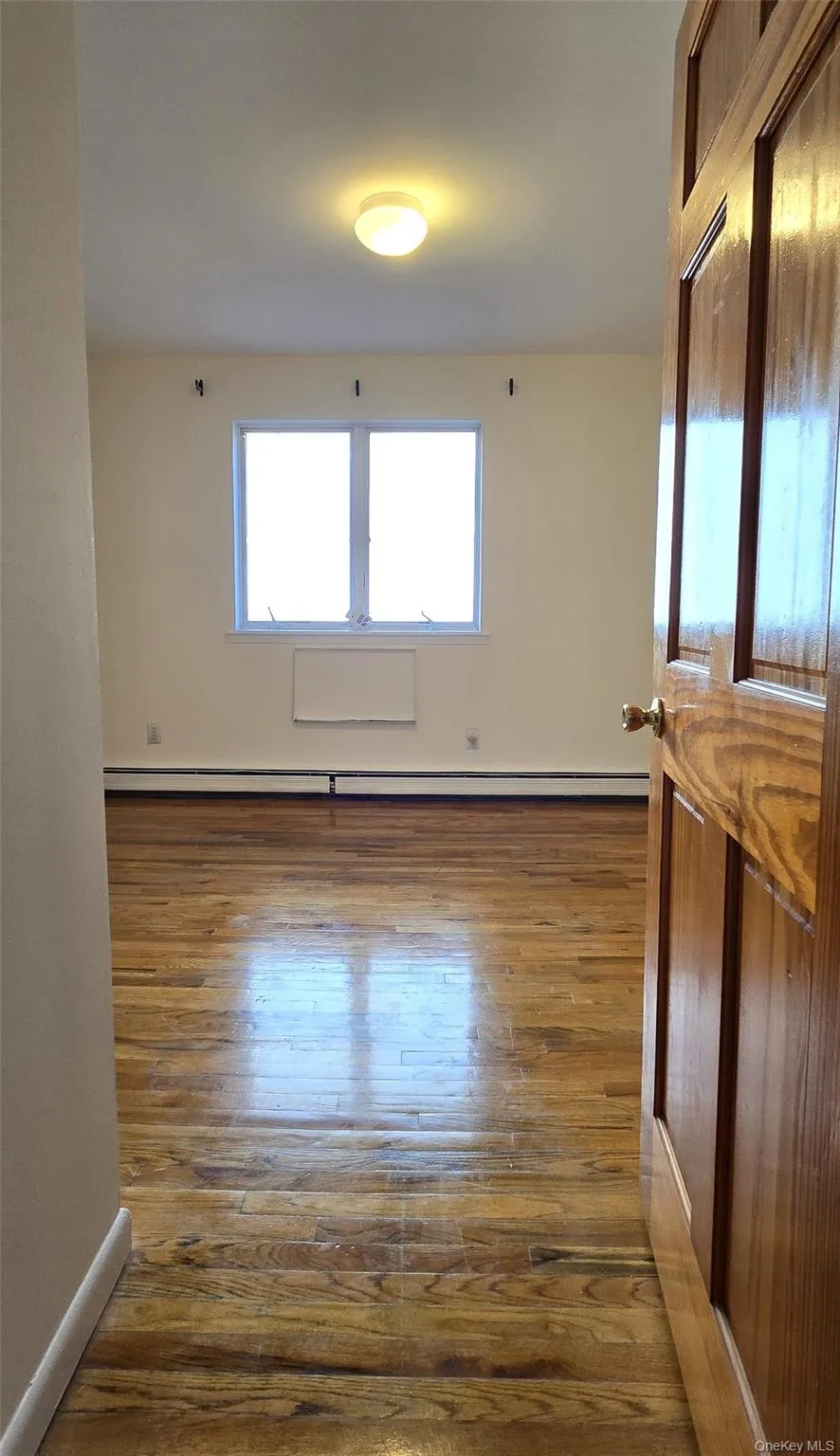 Empty room with dark wood-style flooring and a baseboard radiator Empty room with dark wood-style flooring and a baseboard radiator